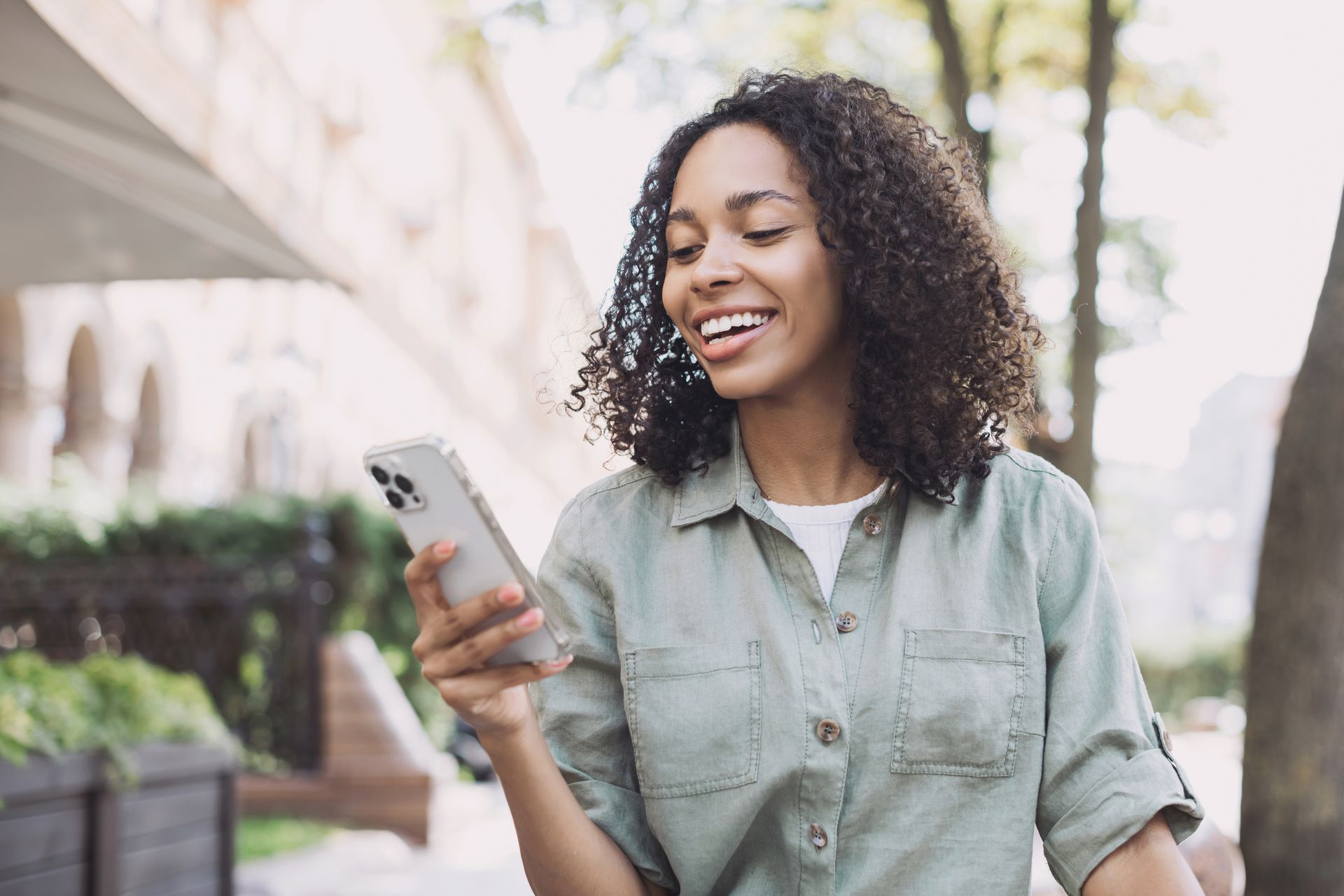 Smiling woman looking at her phone while walking outdoors in a light green shirt