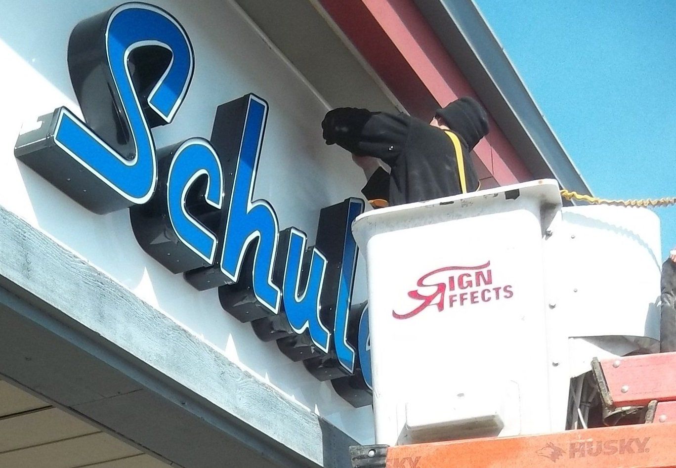 Worker on lift installing blue “Sushi” sign on a building facade