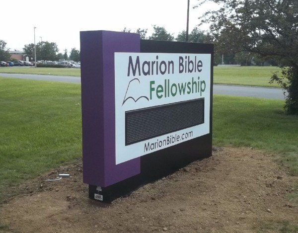 Marion Bible Fellowship sign with purple sides beside a roadside lawn
