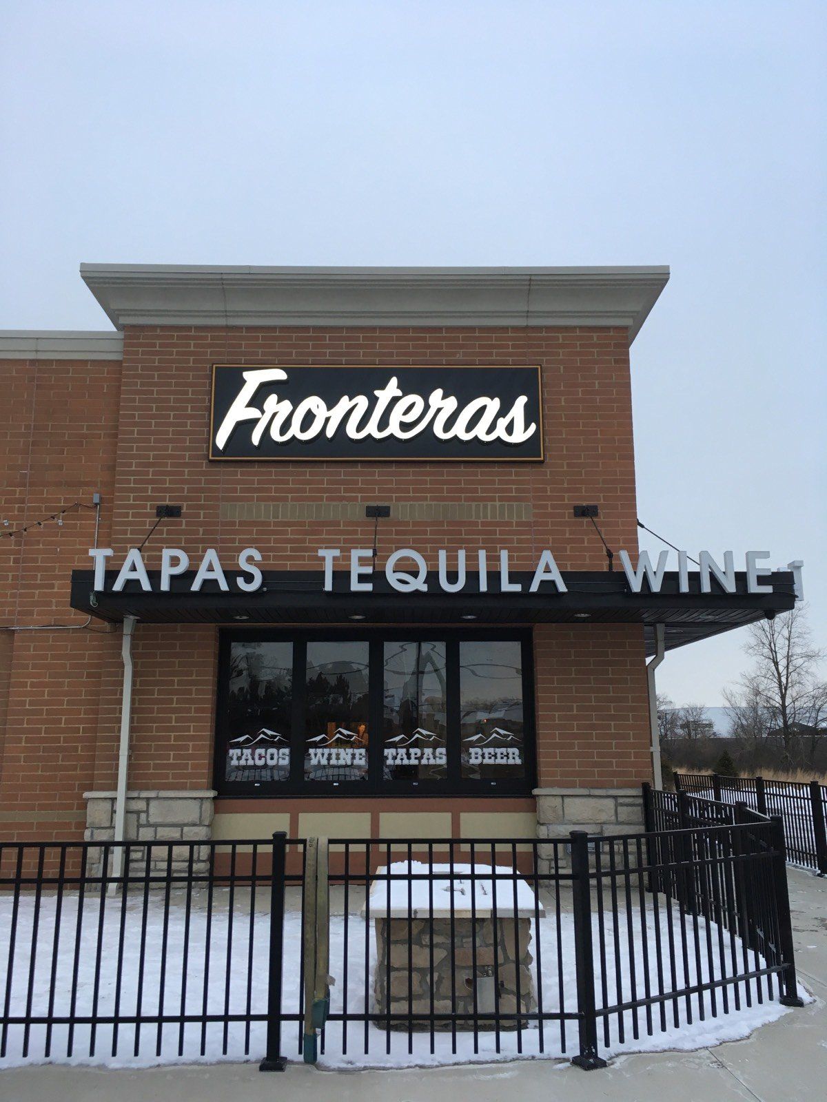 Fronteras restaurant storefront with sign reading “TAPAS TEQUILA WINE” and a snowy fence in front