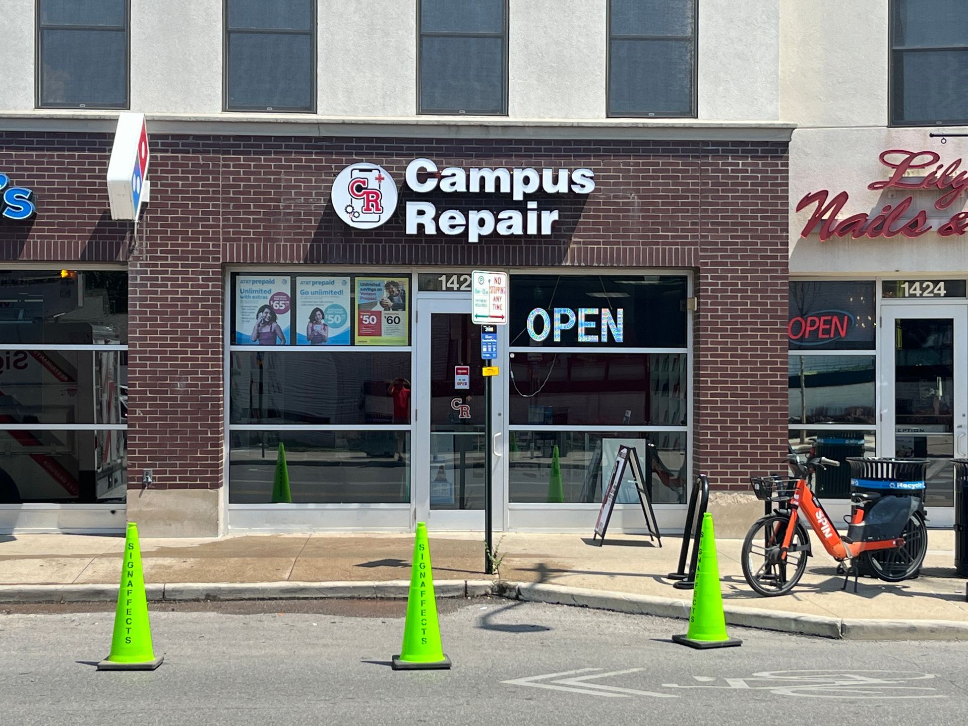 Storefront of Campus Repair with open sign, brick facade, and orange scooter parked outside.