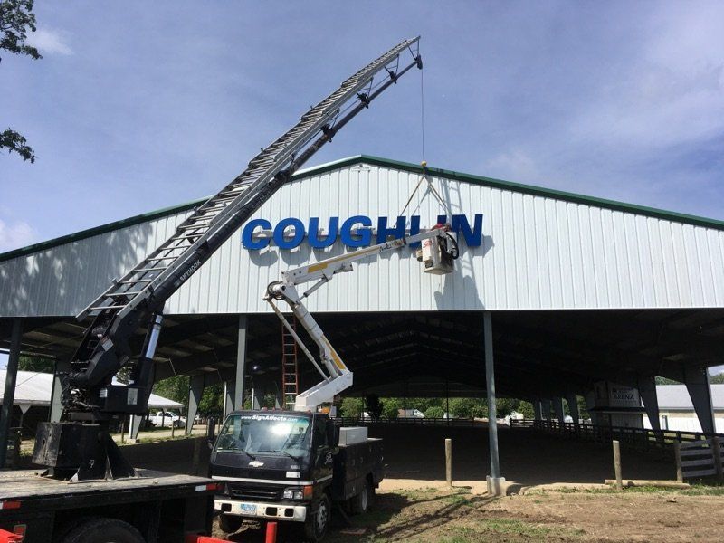 Two boom lifts working on a white building with blue Coughlin sign