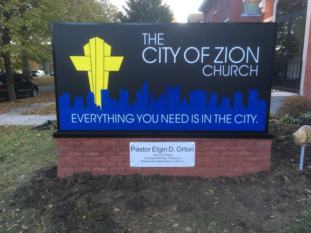 Sign for The City of Zion Church with blue skyline graphic and “Everything you need in the city” slogan