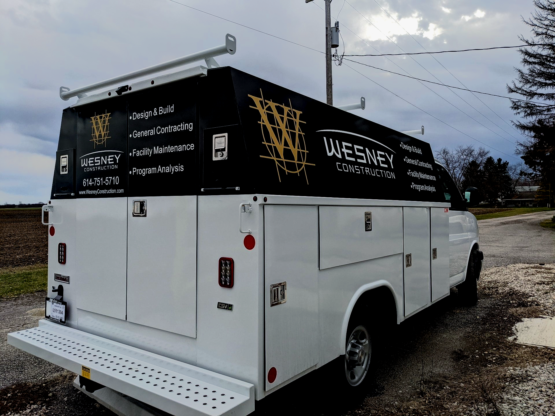 White utility truck with black “WESNER” signage parked on gravel under a cloudy sky