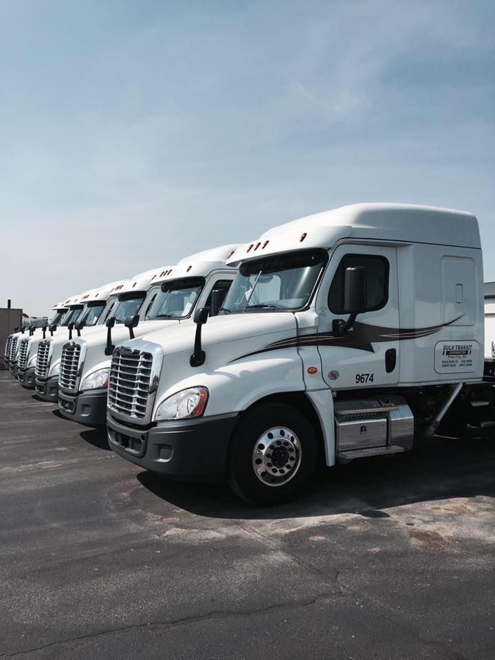Row of white semi-trucks parked in a lot under a clear sky