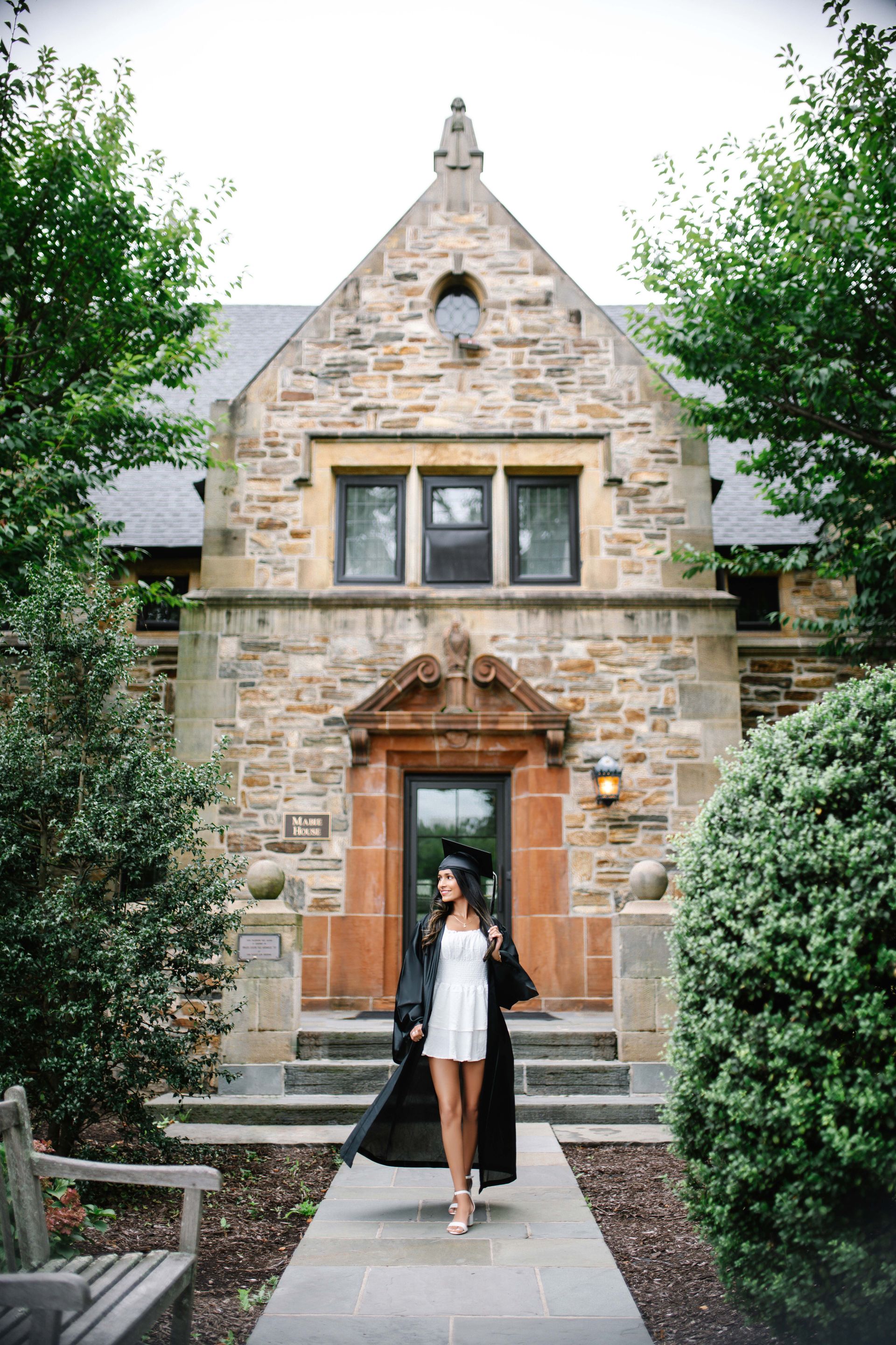 Woman in graduation gown walks towards stone building.