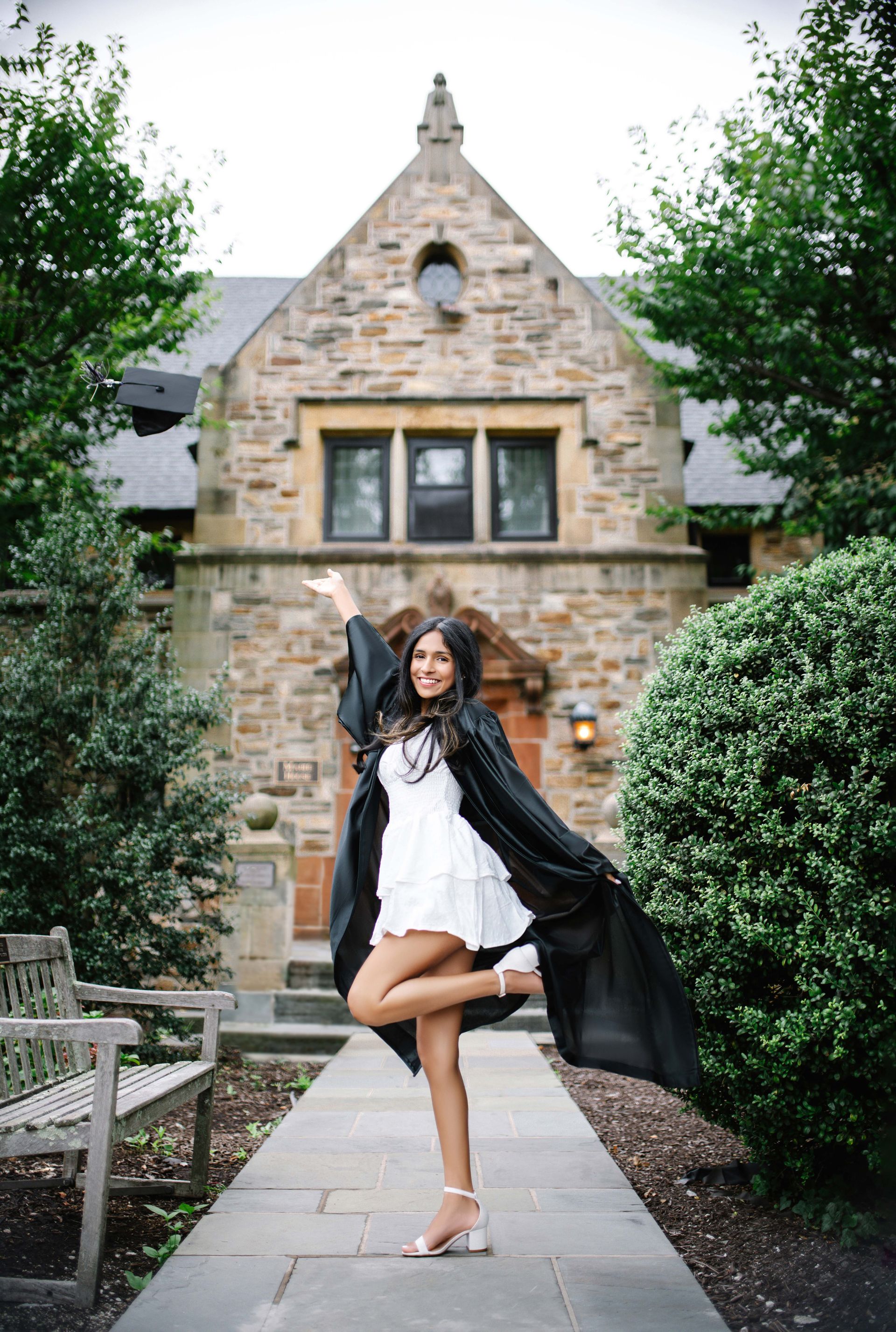 Woman in cap and gown poses playfully in front of a stone building.