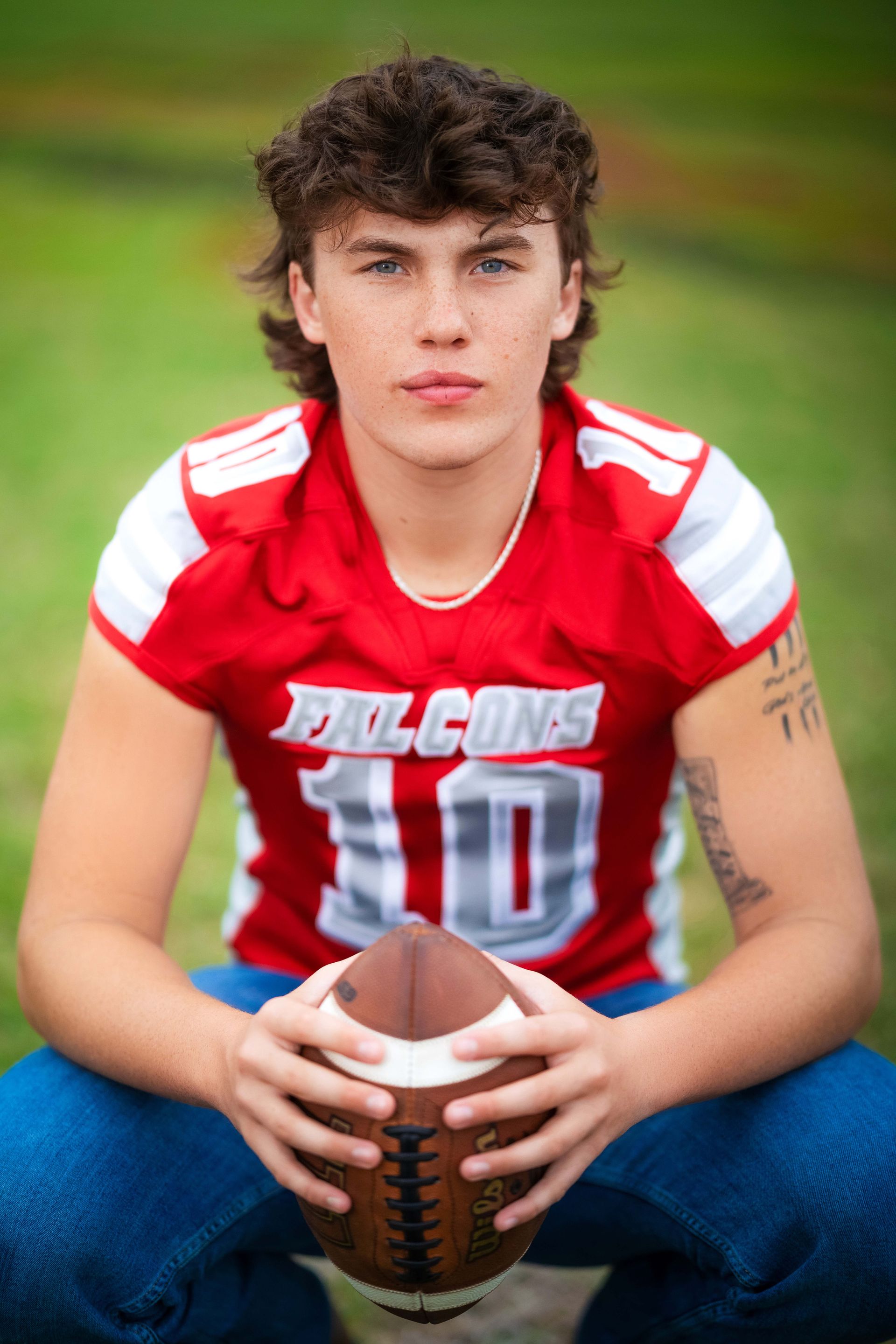 Football player in red jersey, number 10, holding ball. Green grass, looking at camera.