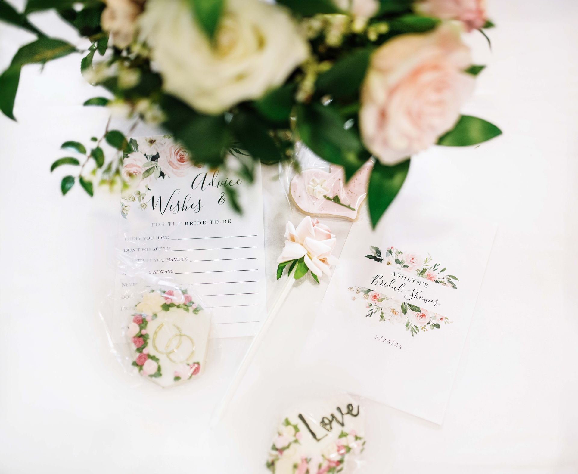 Wedding decor: flowers, wishes sign, cookies, and a card on a white surface.