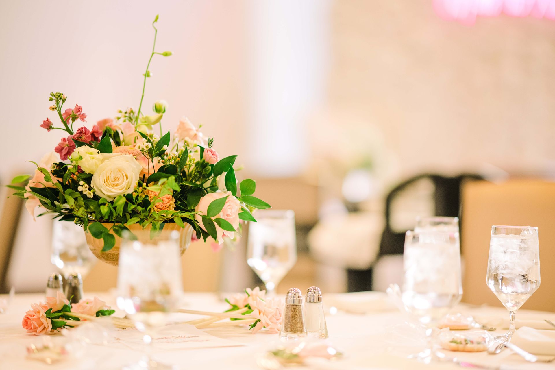 Elegant floral centerpiece on a table set for a formal event, with glasses, and a salt and pepper shaker.