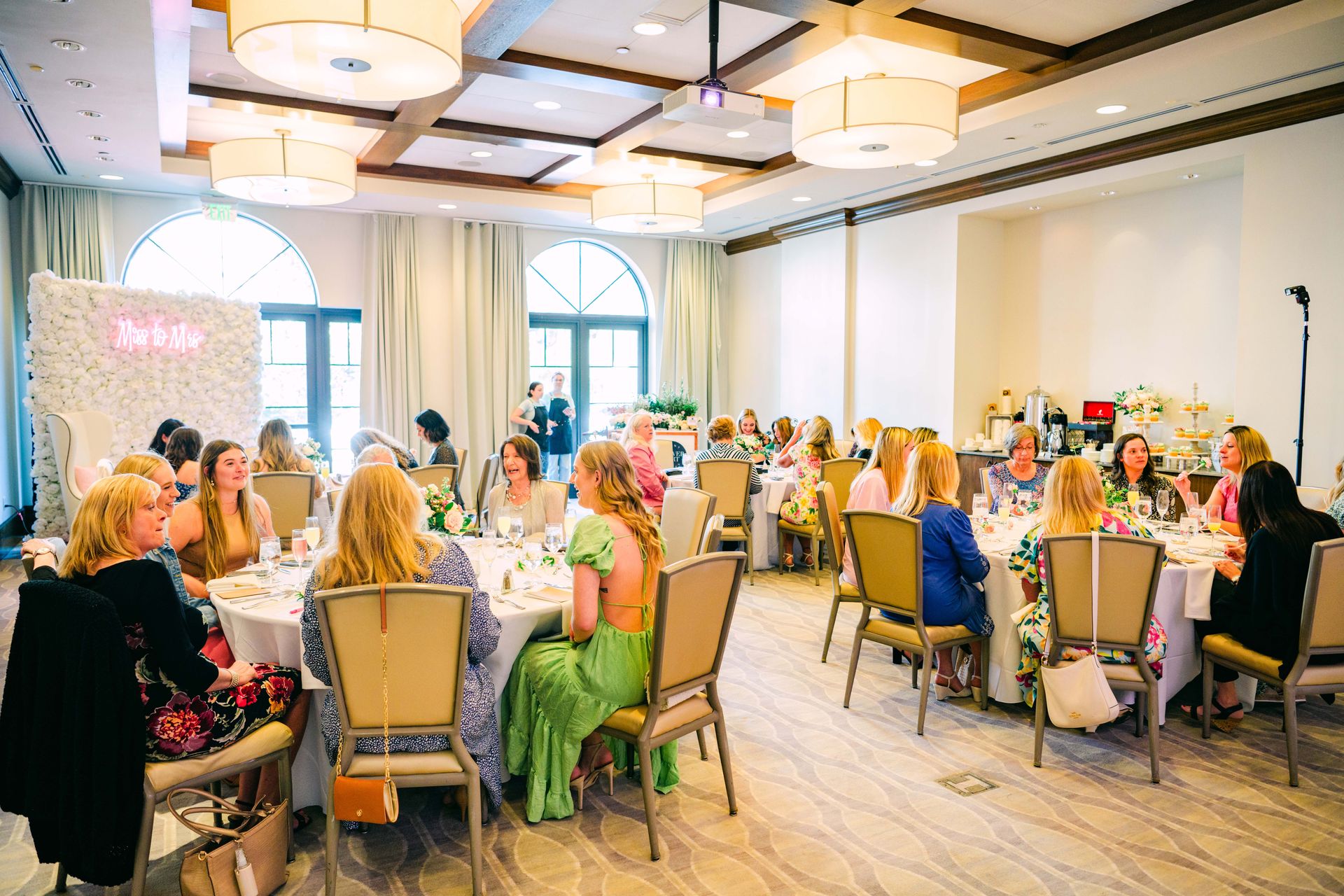 A bridal shower in a bright room with many women seated at round tables.