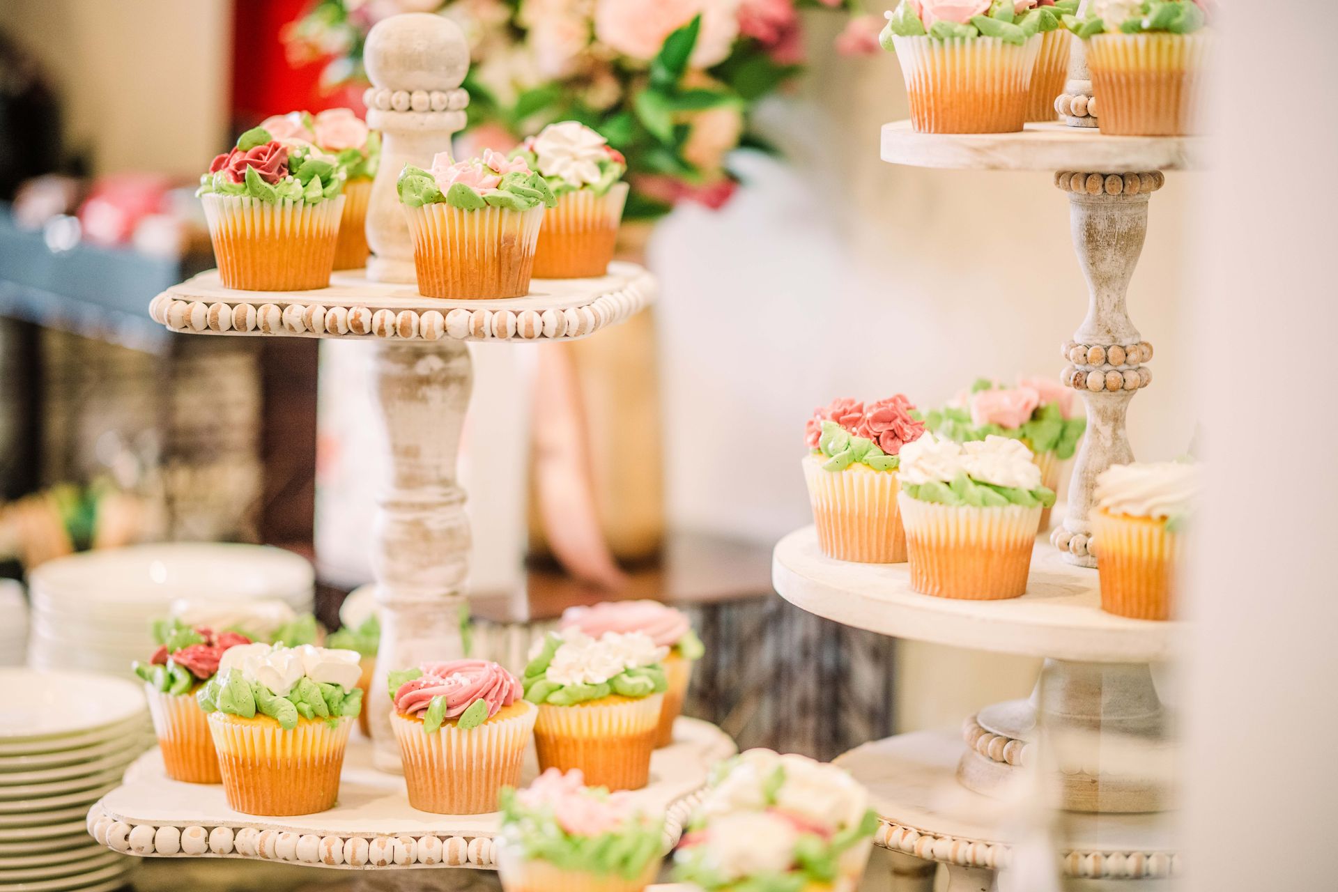 Cupcakes with floral frosting on tiered white stands, set for a party.