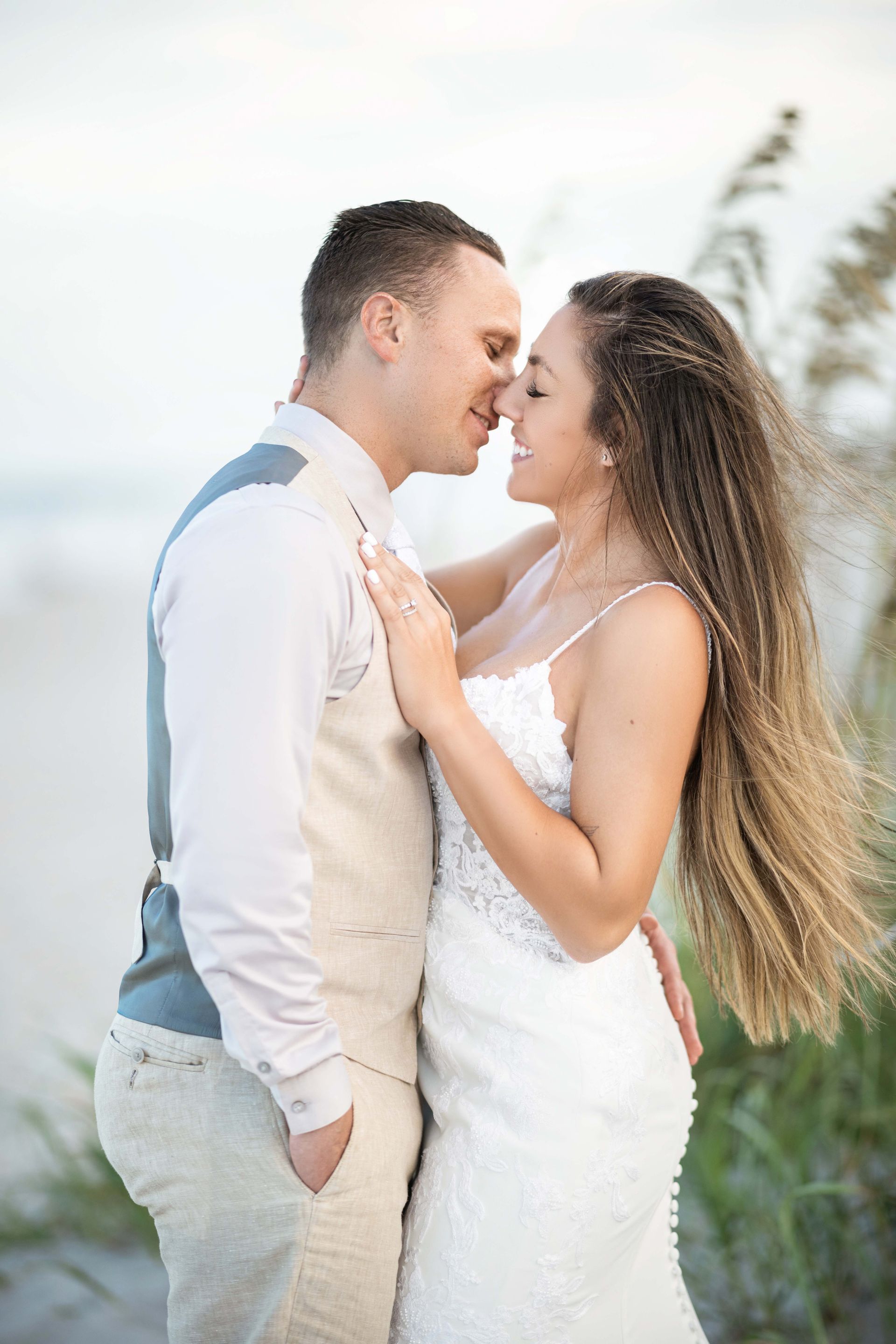 Couple kissing on a beach; bride in a white dress, groom in a vest.