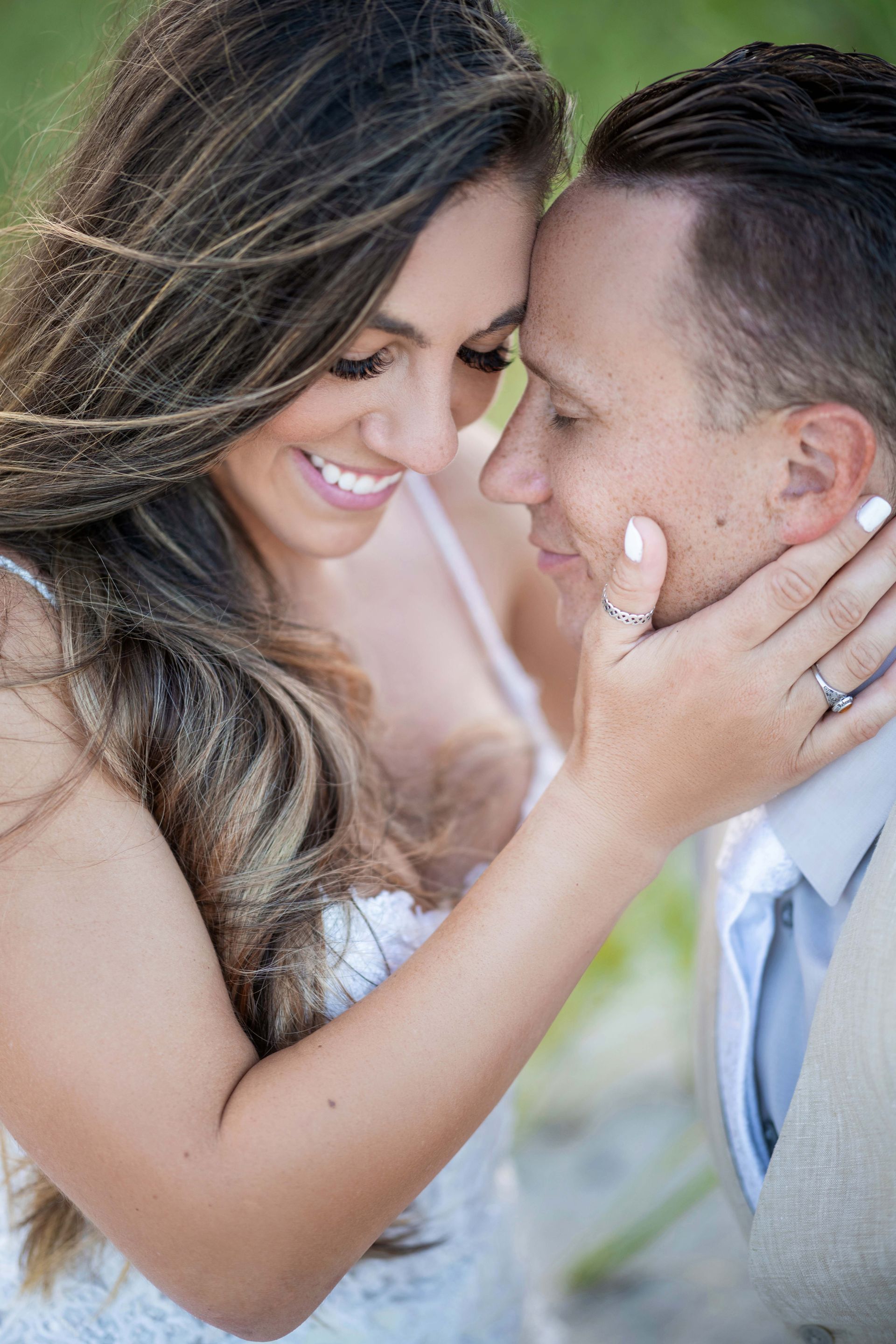Smiling couple embracing, woman touching man's face, outdoors with soft light.