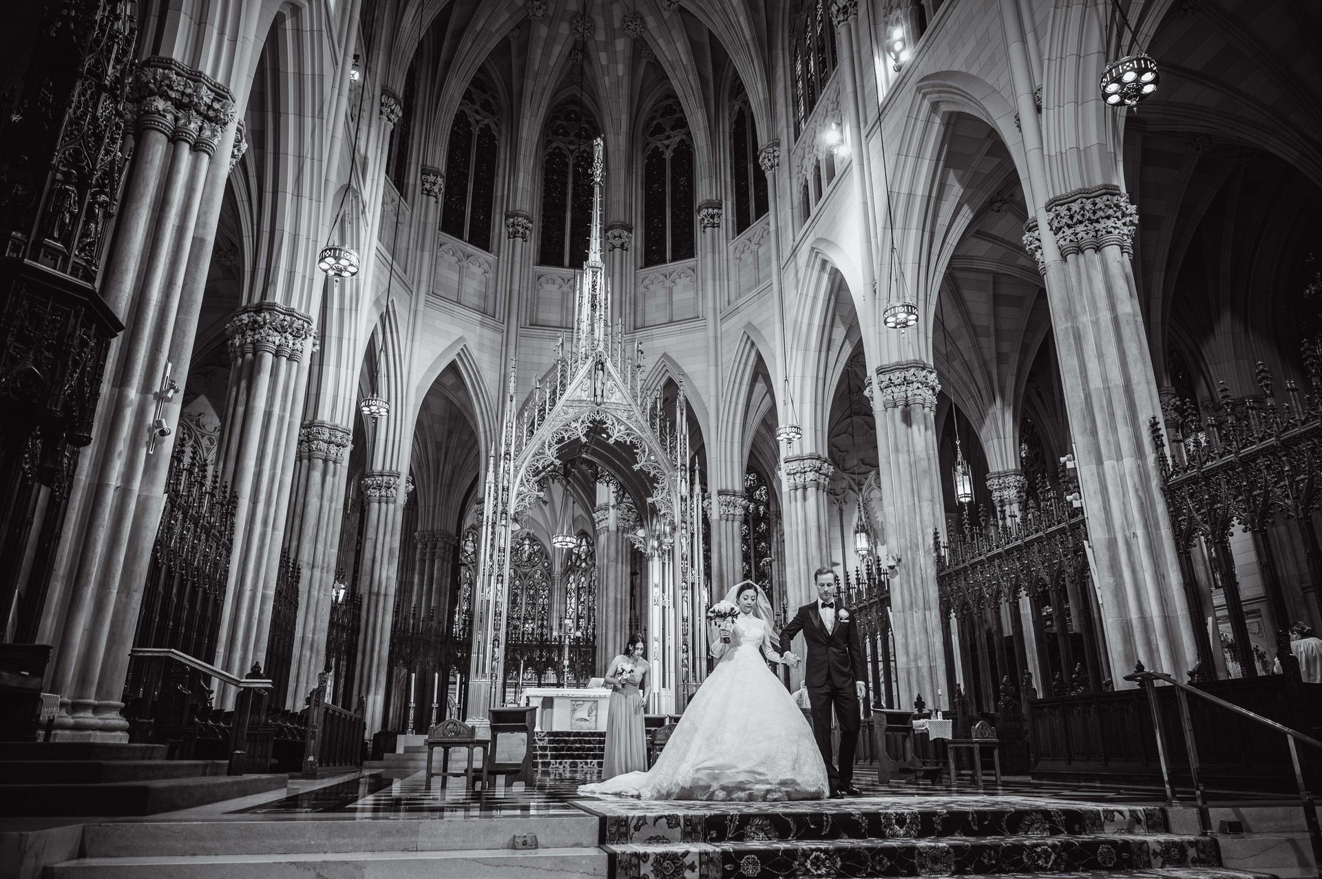 Bride and groom in formal wear celebrating in a grand, gothic cathedral. Black and white photo.