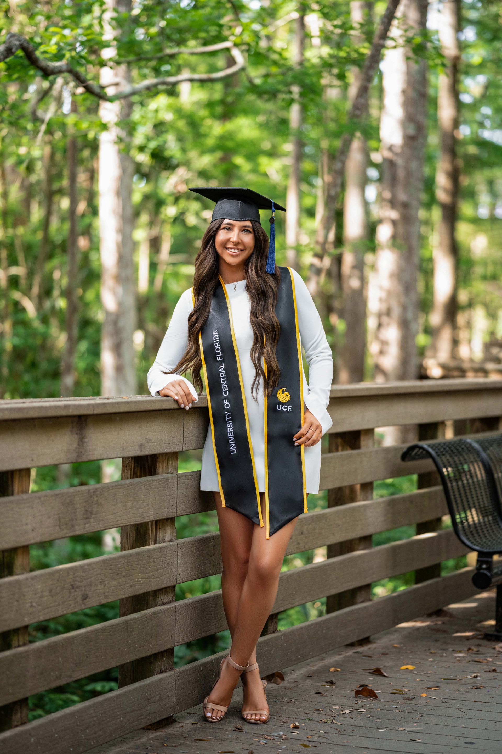 Woman in graduation cap and gown, leaning against wooden railing.