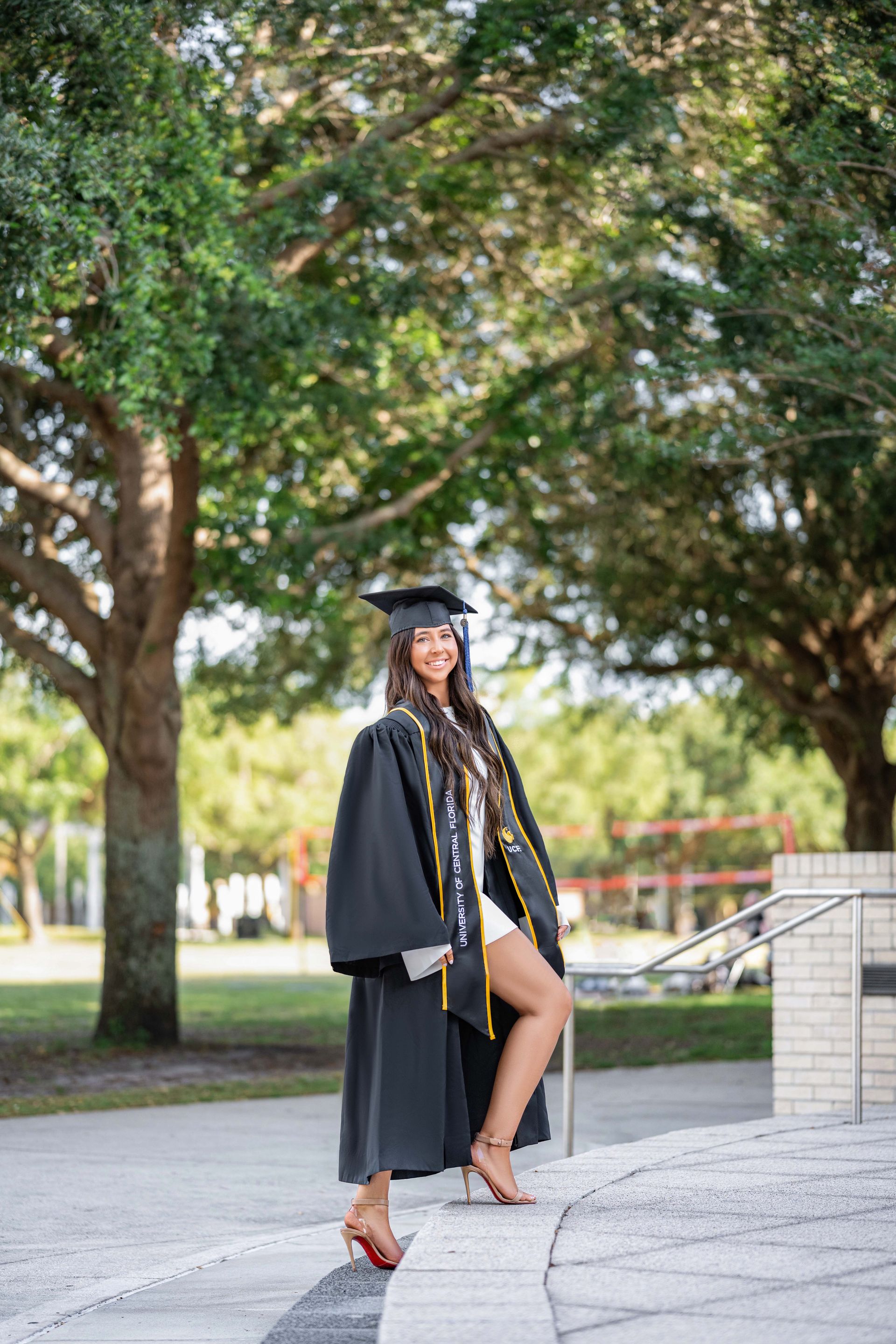 Graduation portrait of a smiling Black woman in cap and gown, standing on steps, outdoors.