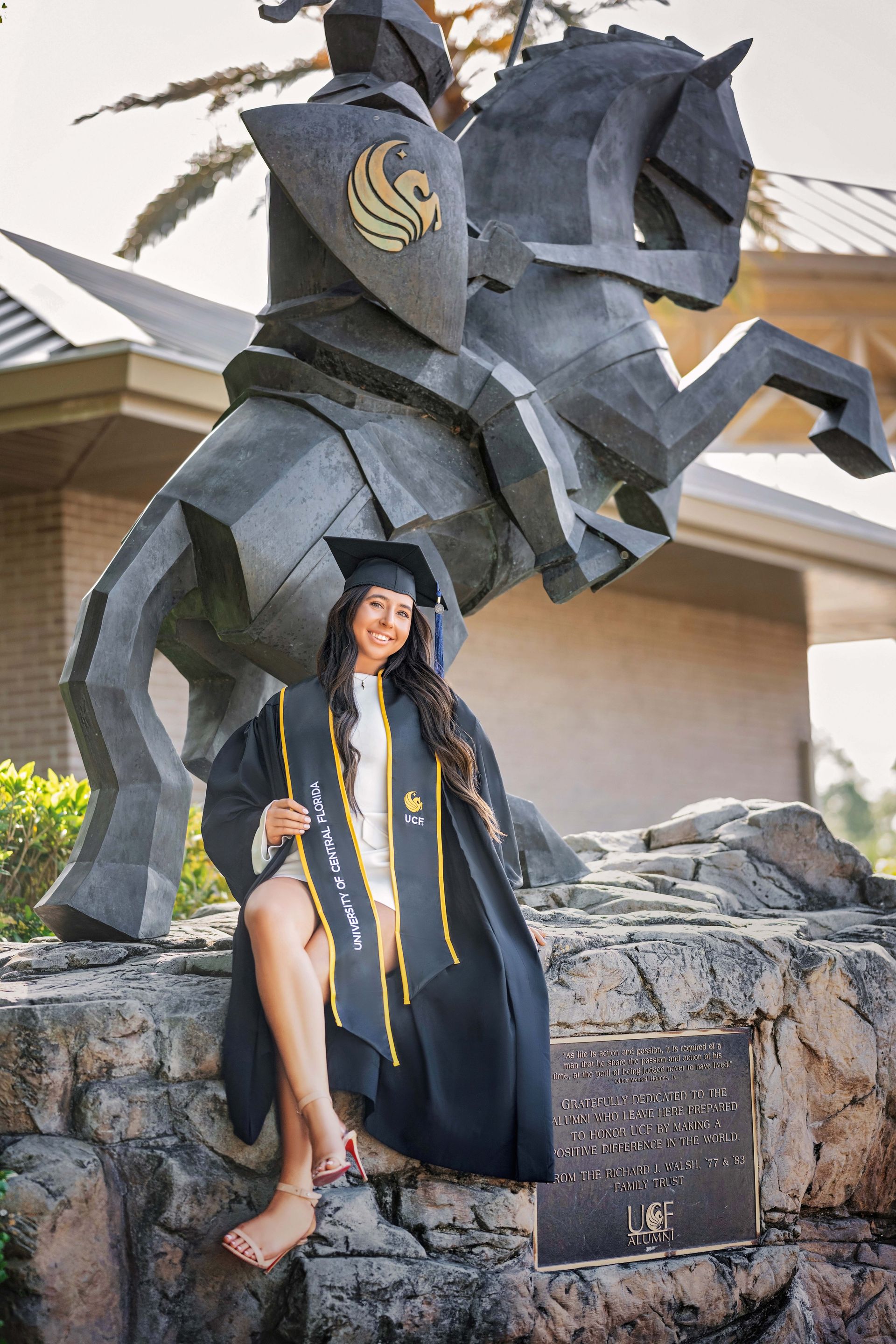 Woman in graduation gown poses by a knight statue.