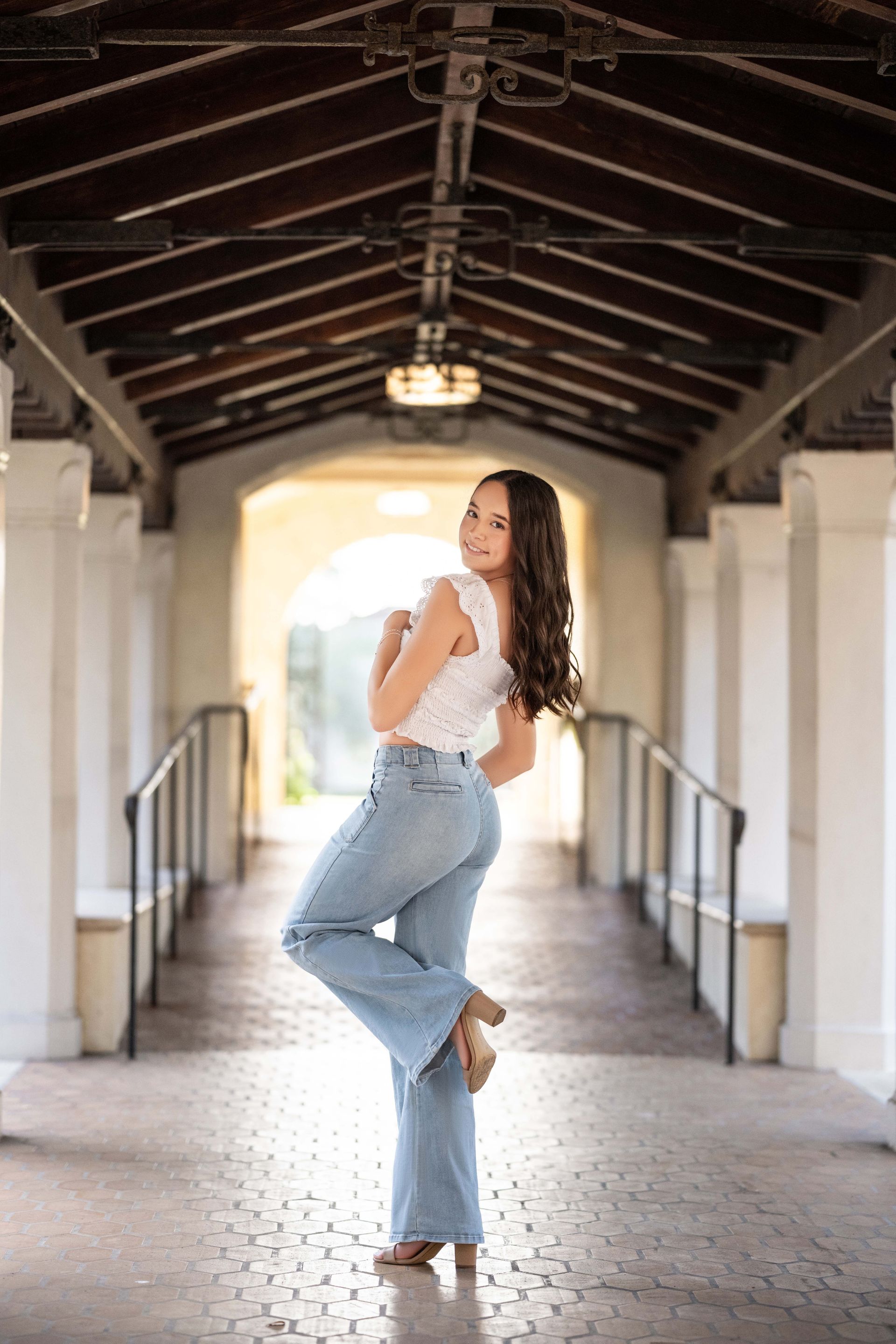 Woman in white top and jeans posing in arched walkway.
