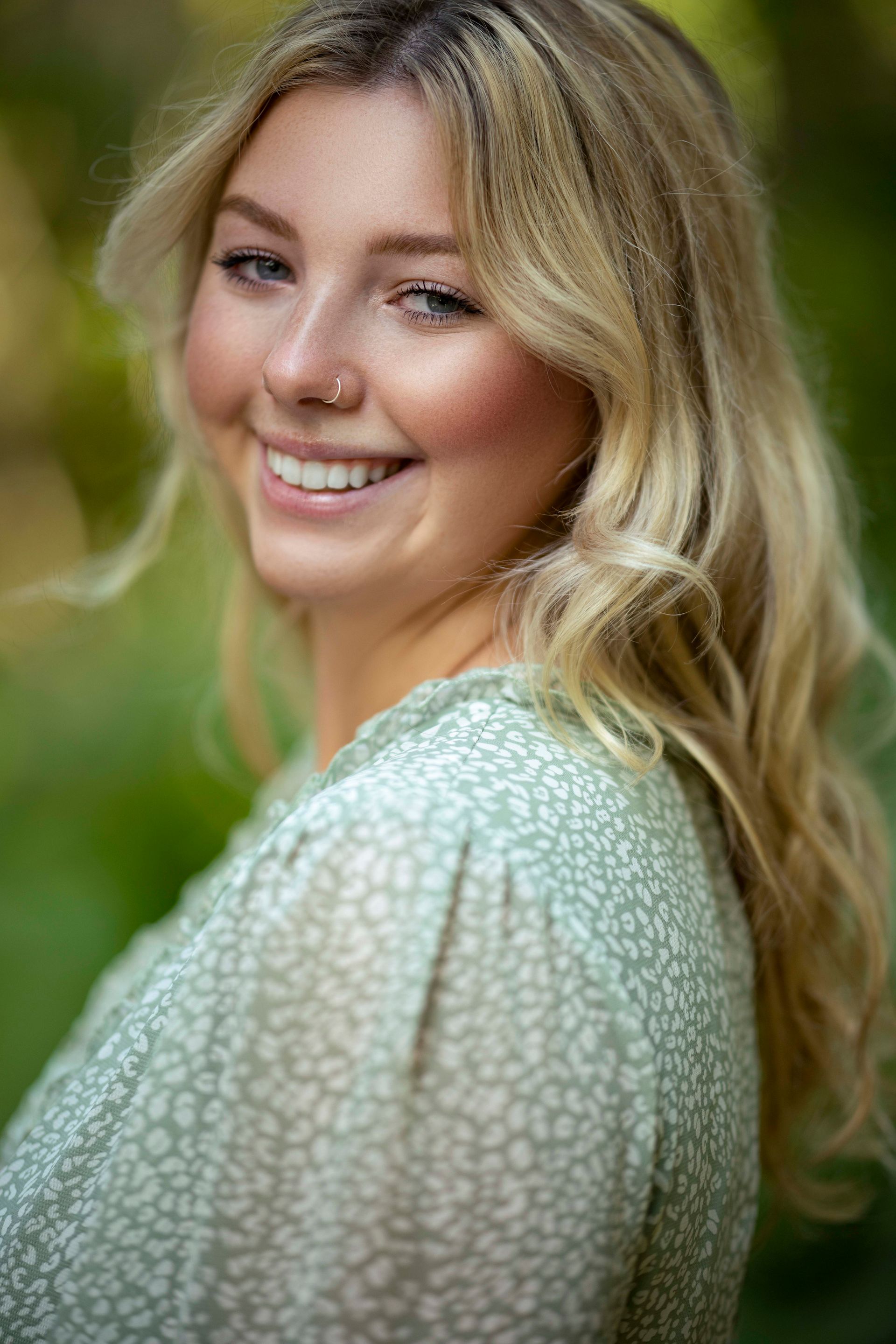 Blonde woman smiles outdoors, wearing a green floral dress.
