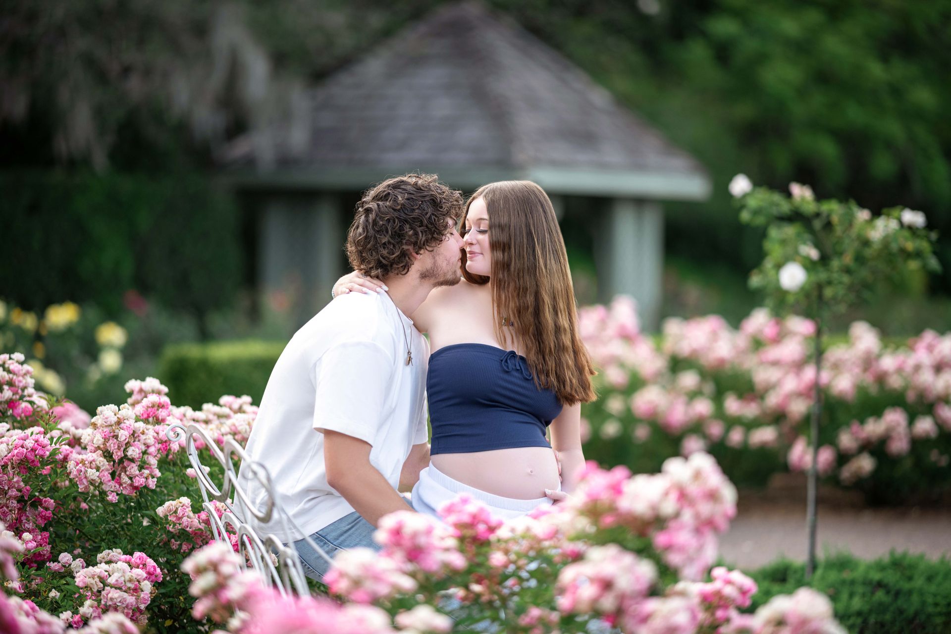 Couple kissing in a rose garden; woman is pregnant.