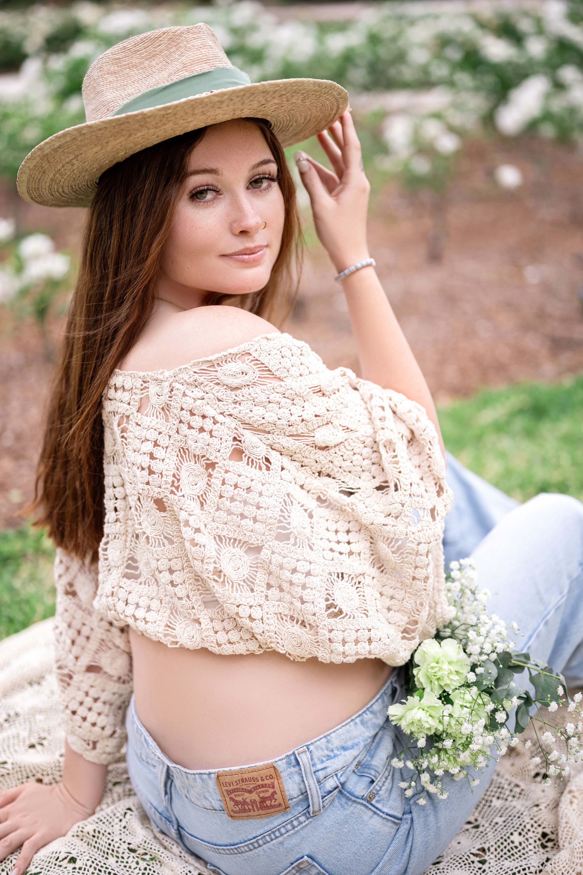 Woman in straw hat and crop top, holding flowers, sitting outdoors.
