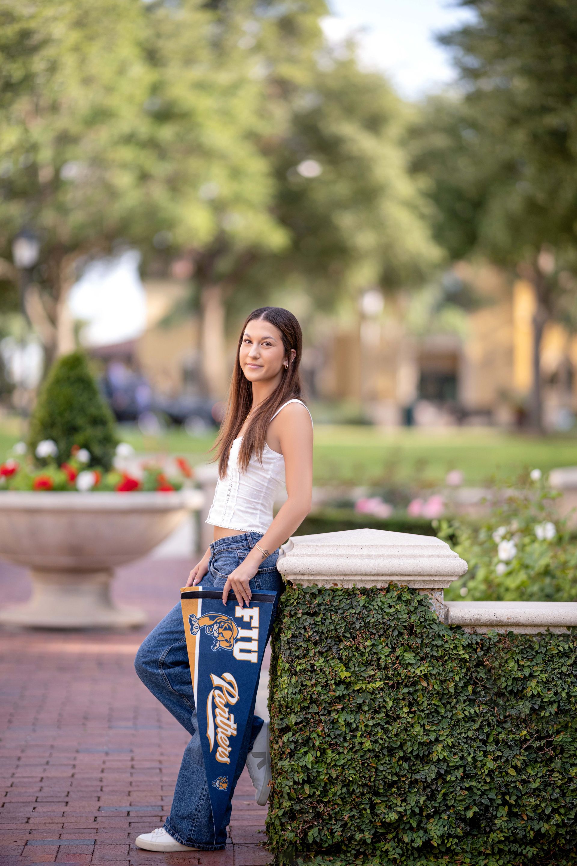 Woman in jeans and white top, leaning on wall, holding a pennant, outdoors.