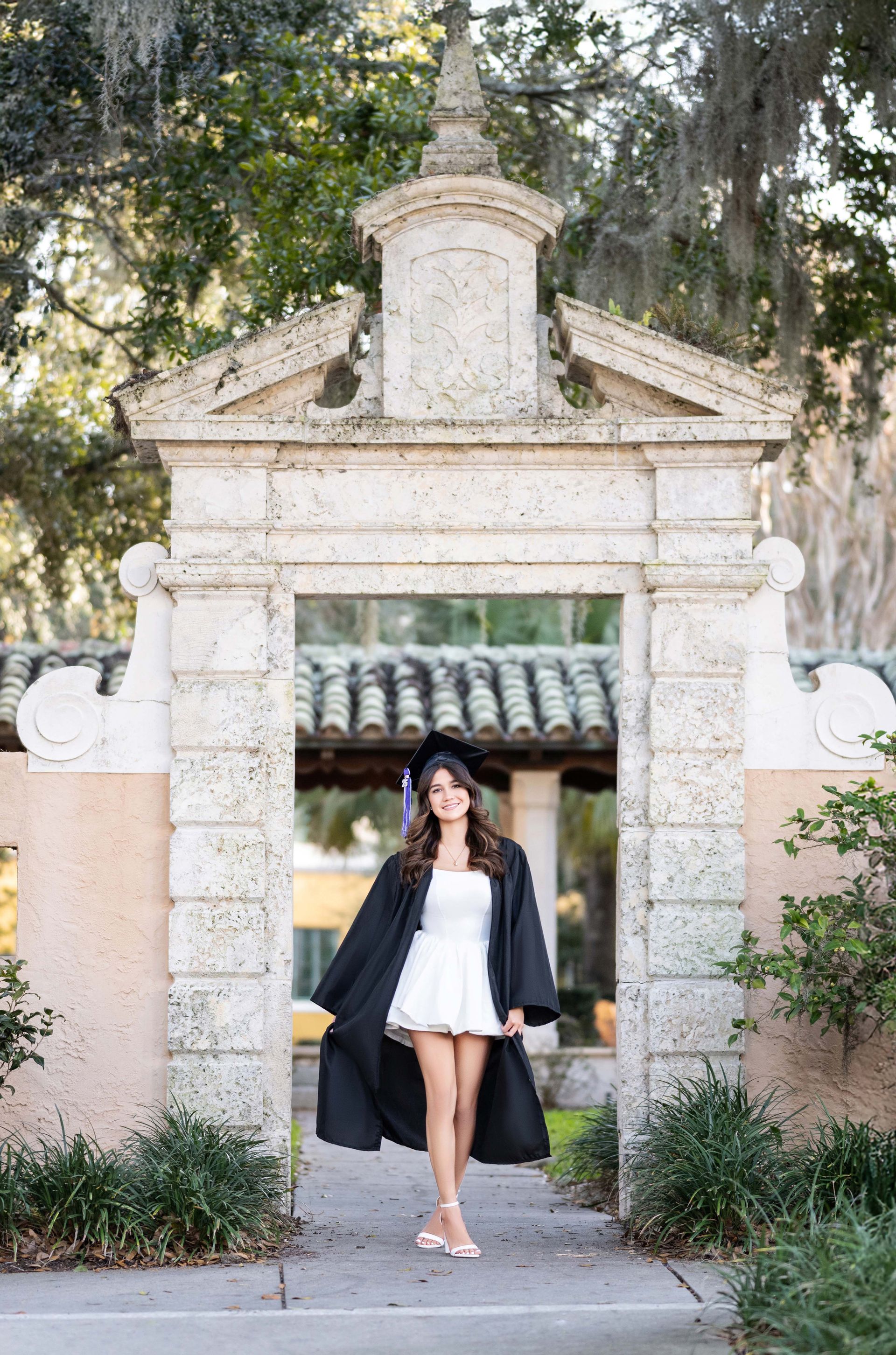 Woman in graduation cap and gown poses in a stone archway.