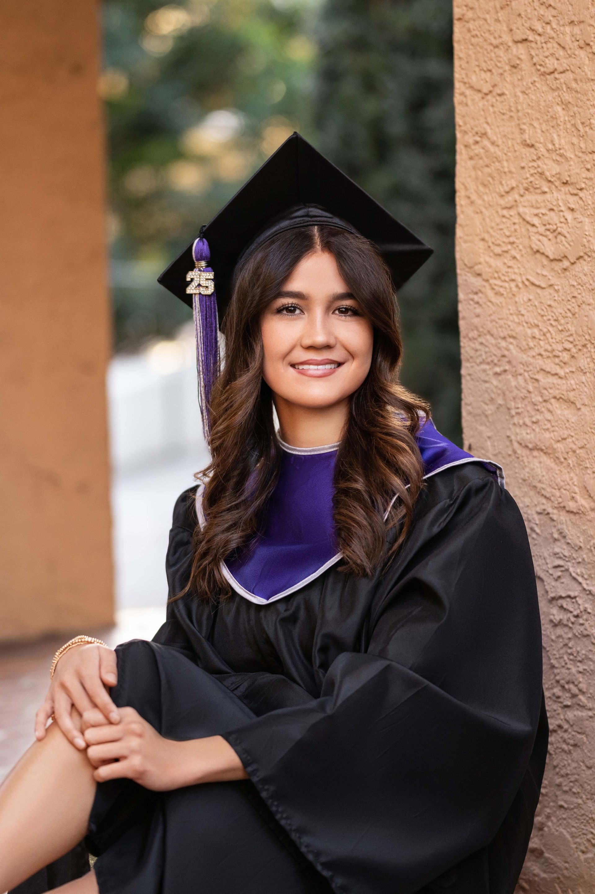 Woman in graduation cap and gown, smiling, outdoors.