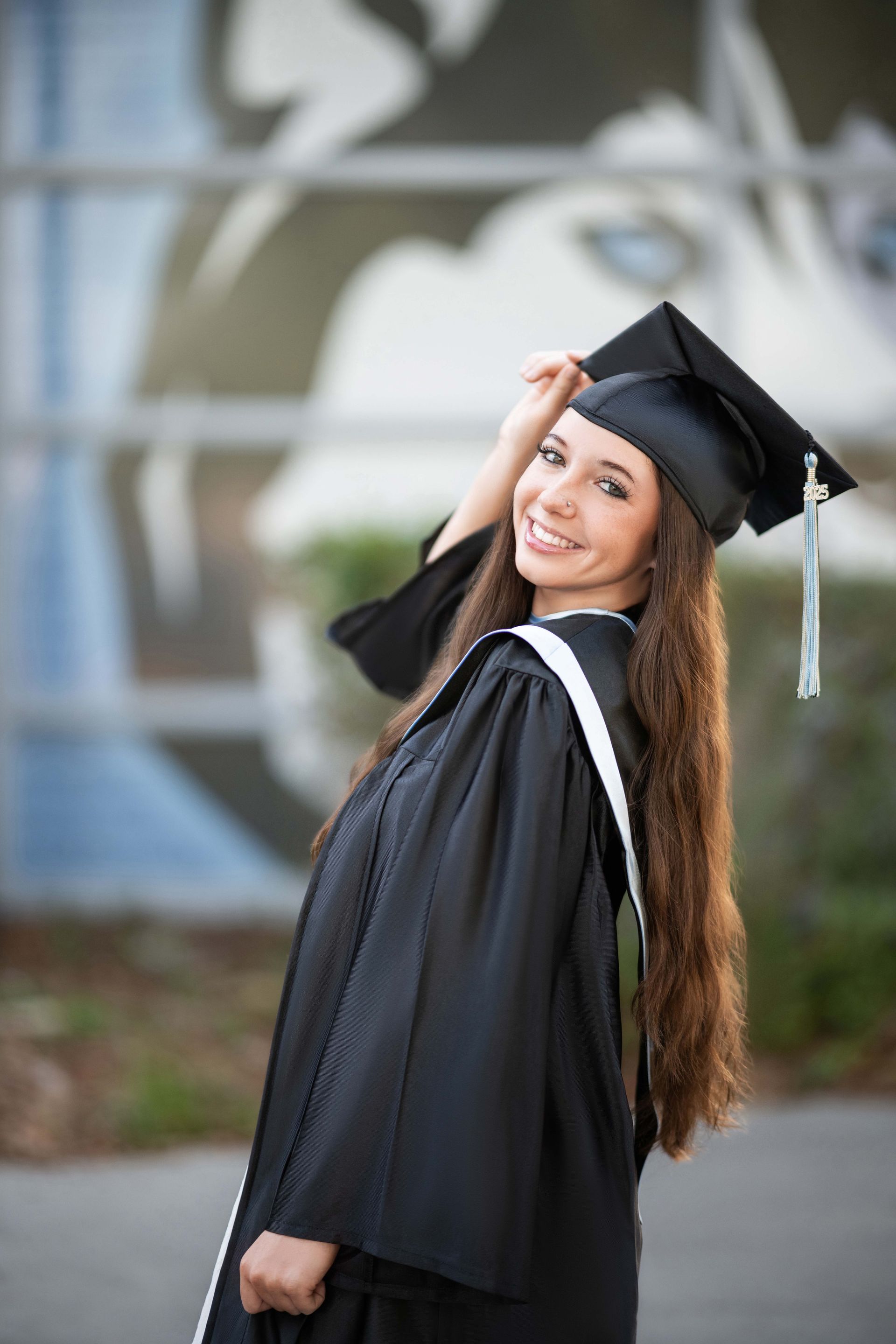Graduation photo: Smiling woman in cap and gown, looking over her shoulder, long brown hair.