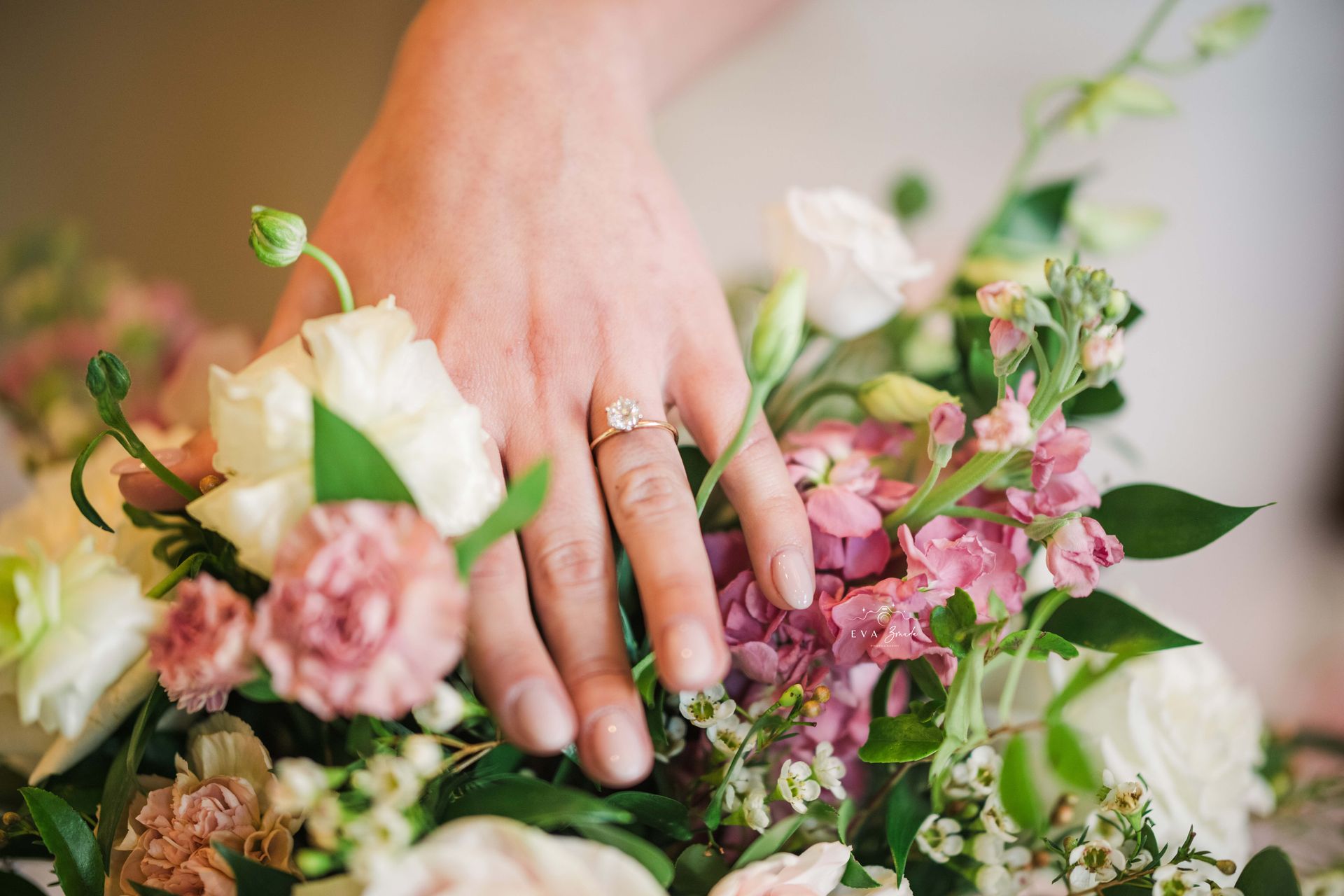 Hand with engagement ring on a floral bouquet, with pink and white flowers.
