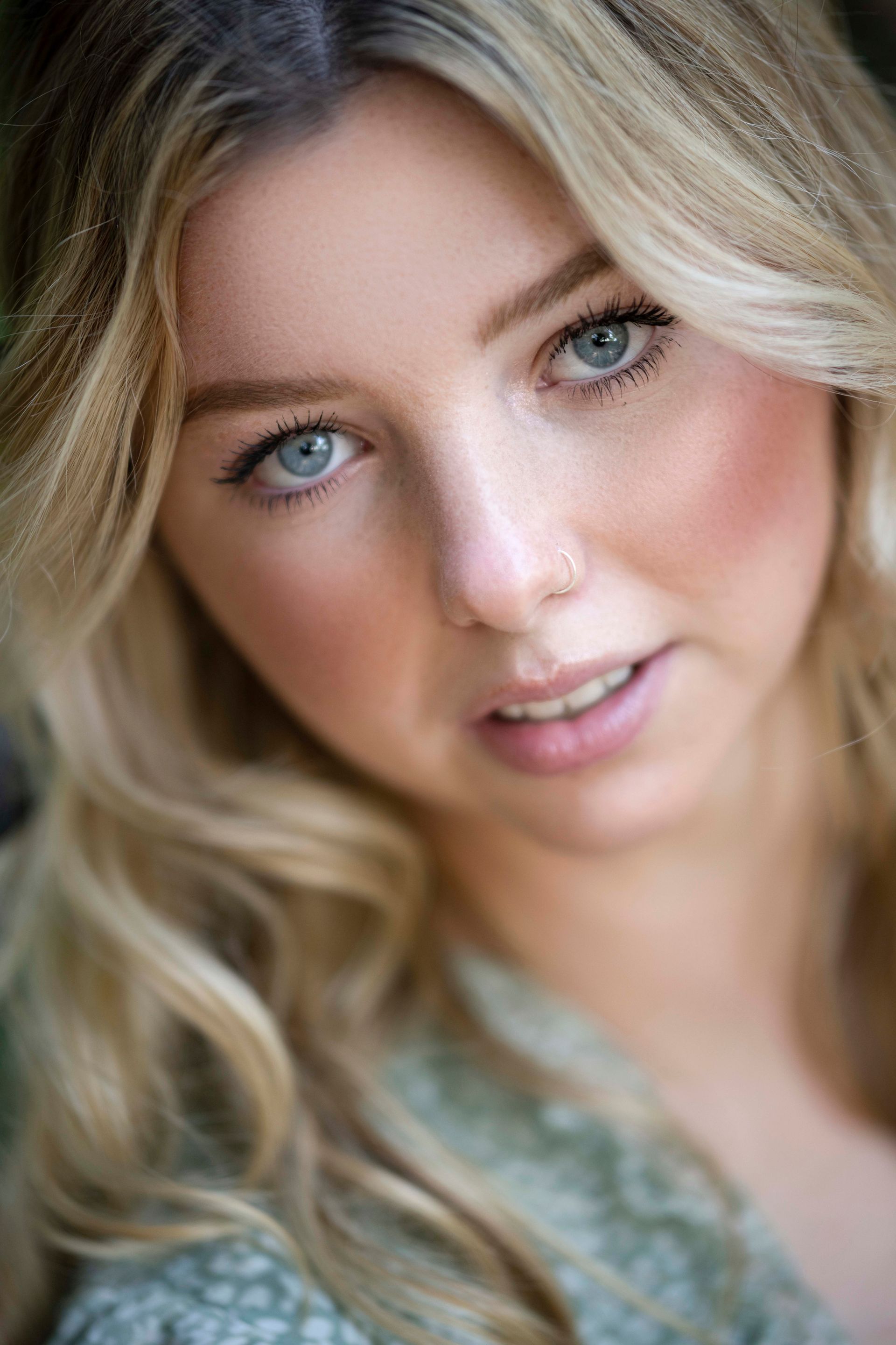 Blonde woman with blue eyes gazes towards the camera, with a soft expression.