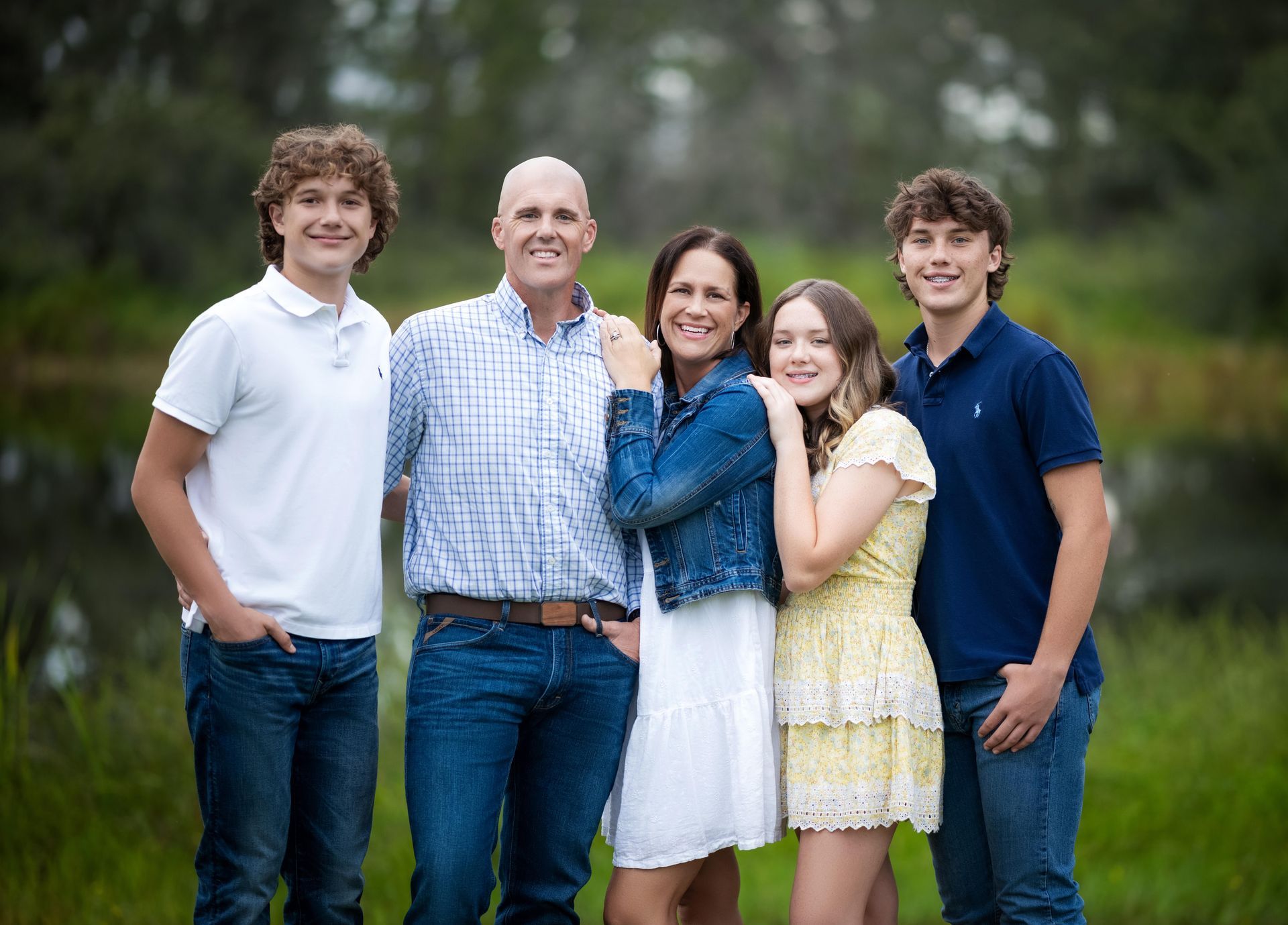 Family of five posing outdoors, smiling and standing close together in casual clothes.