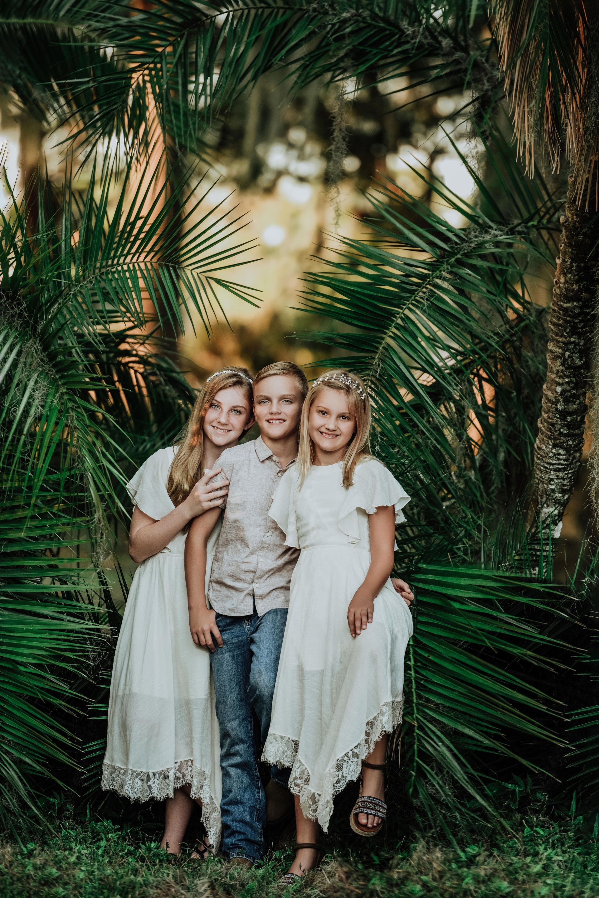 Three children standing together in a lush green garden, smiling at the camera.