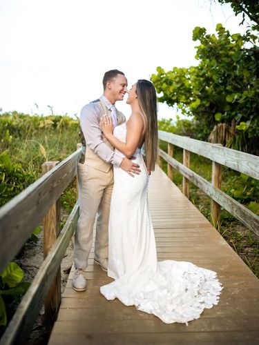 Couple embracing on a wooden boardwalk in wedding attire, surrounded by greenery