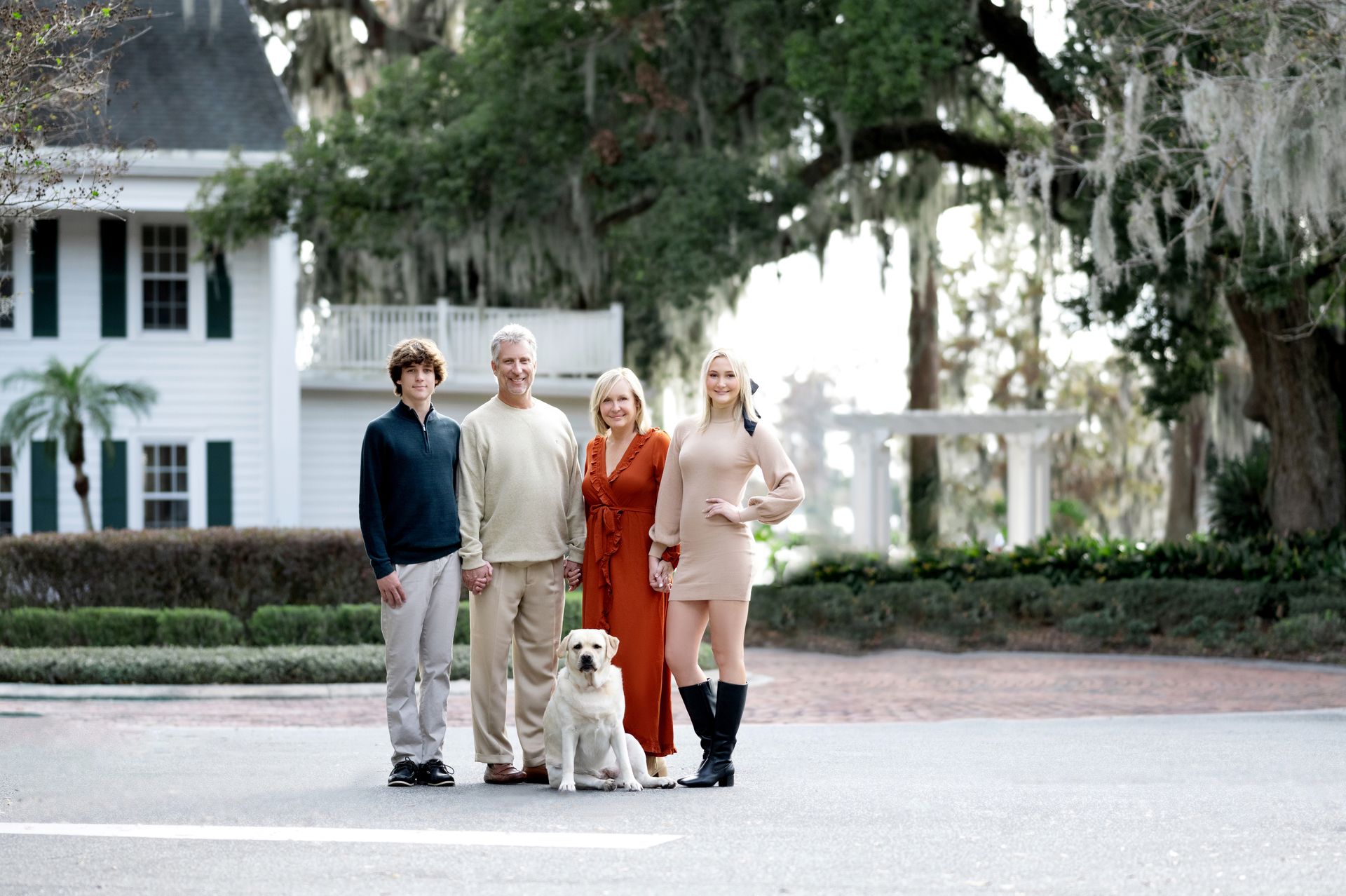Family posing outdoors with a dog in front of a large house
