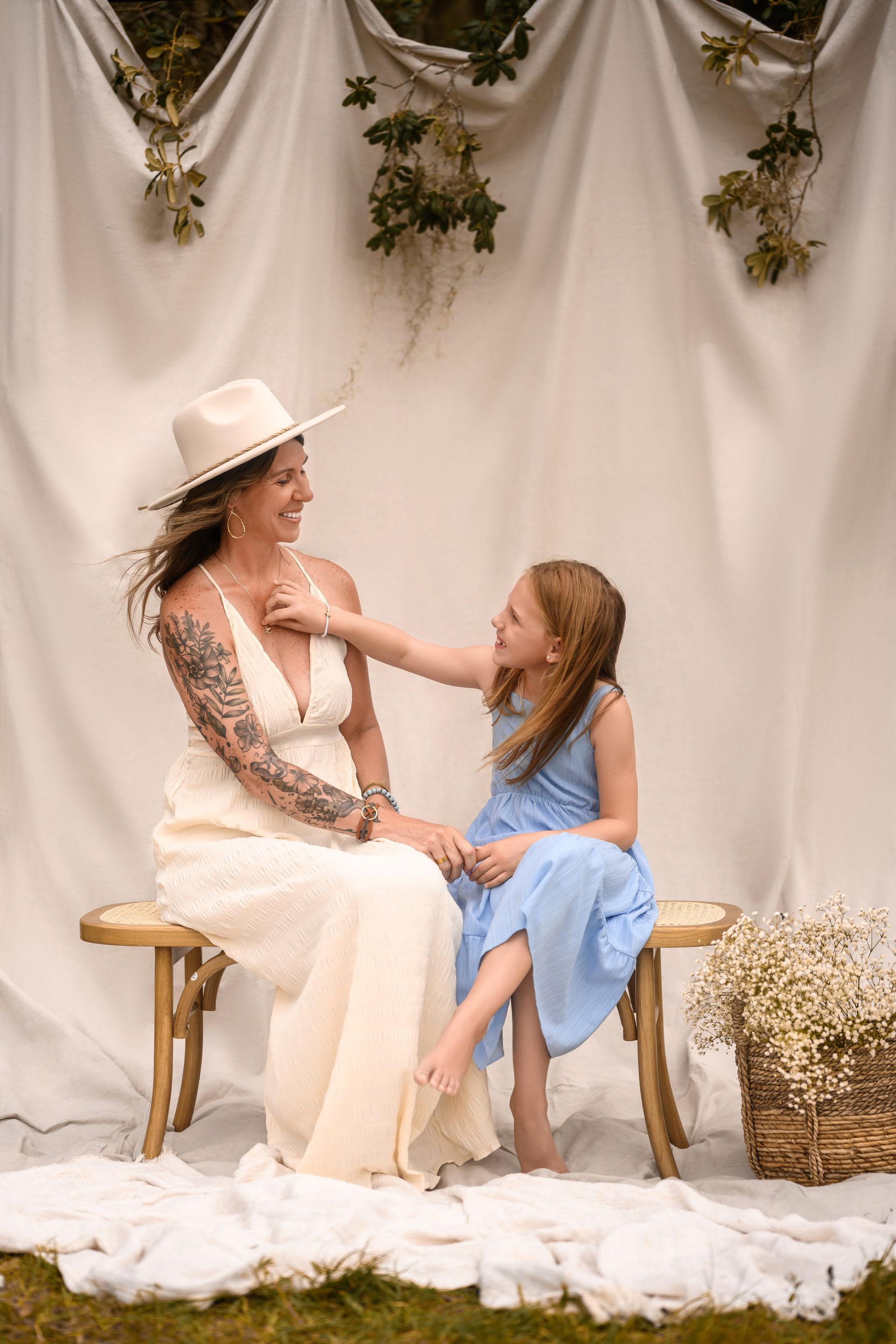 Woman in a white hat and child in blue sitting on a bench in a soft, draped floral studio backdrop