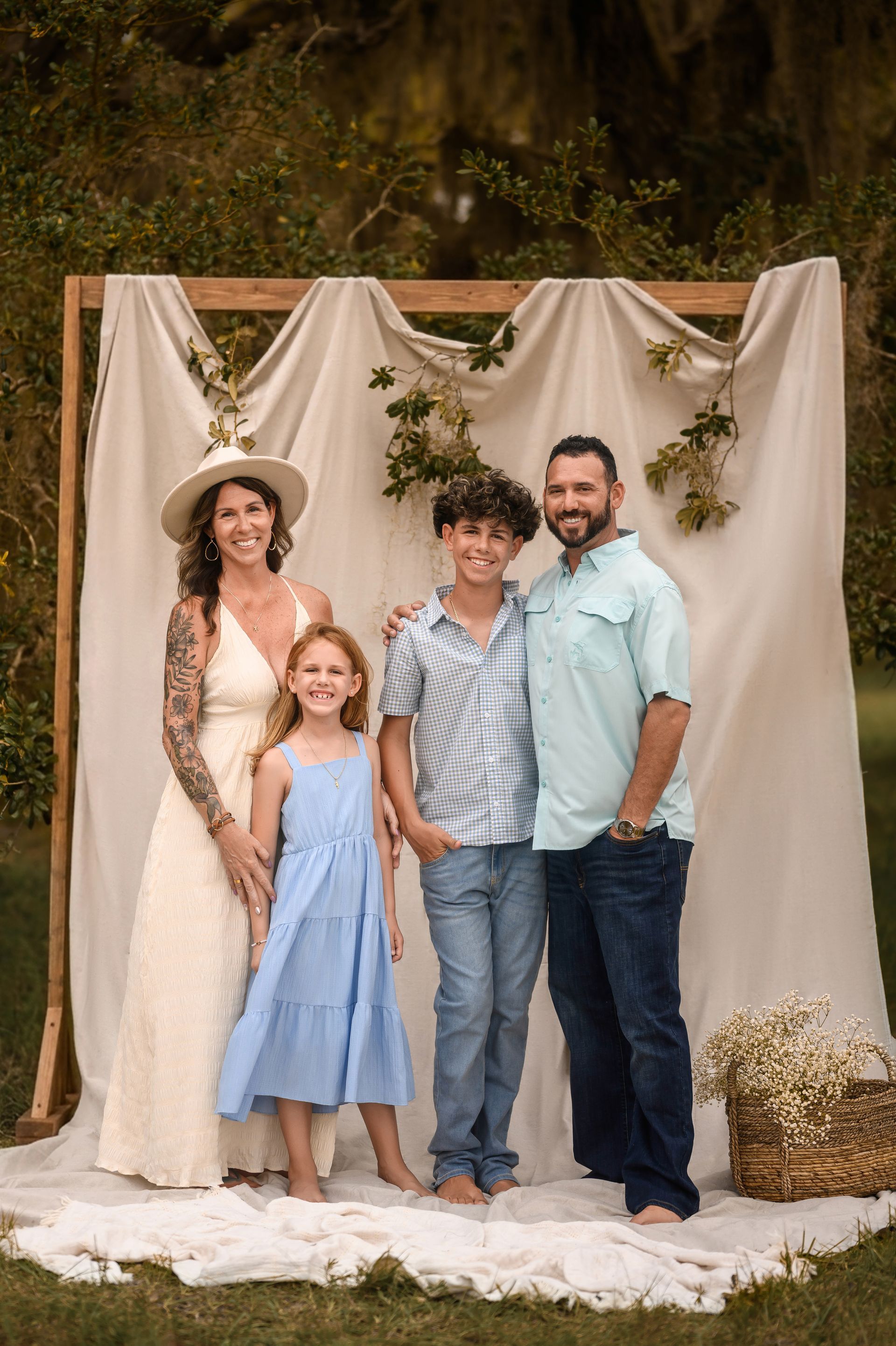 Four people posing in front of a draped outdoor backdrop, wearing light-colored summer clothes.