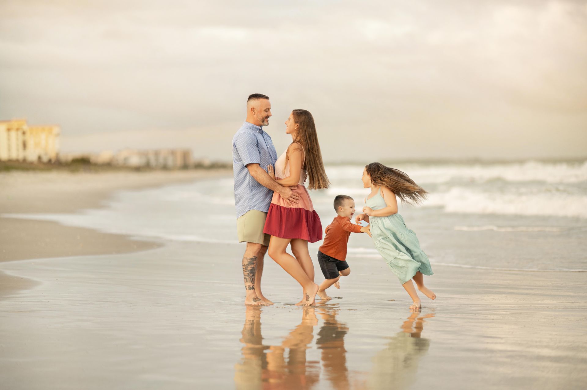 Family running along a wet beach at sunset, with waves and city buildings in the distance