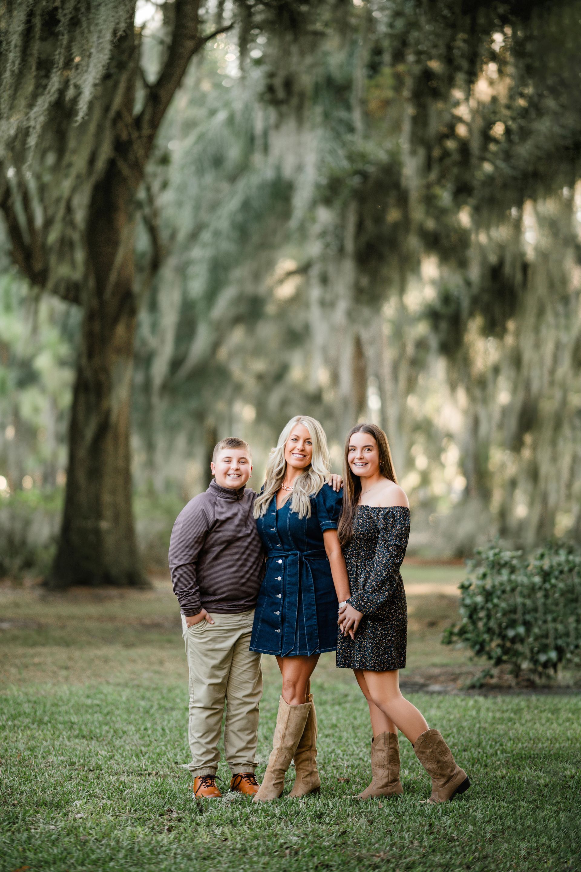 Three women standing together outdoors on grass, posing in front of hanging trees.