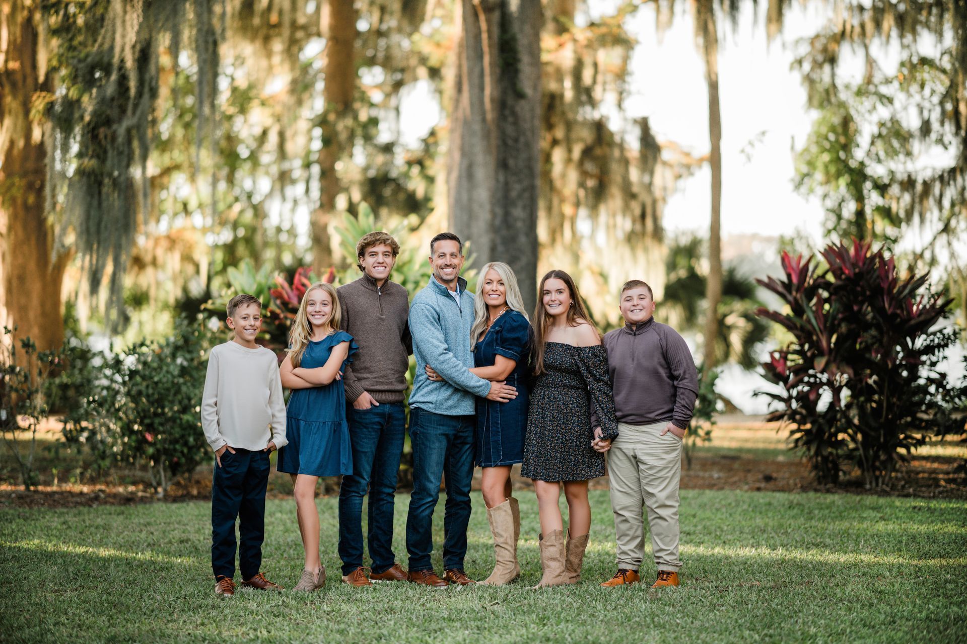 Group of seven standing together outdoors in a garden, smiling at the camera.