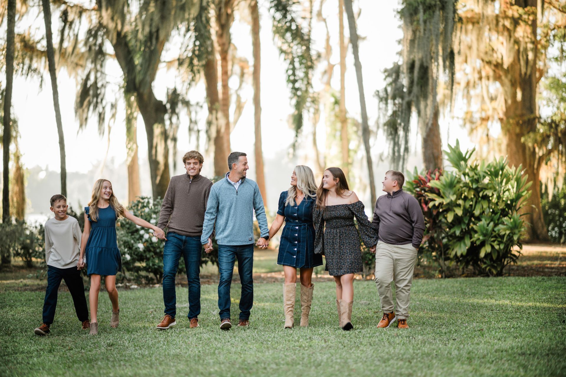 Group of people standing and chatting on a grassy lawn with trees in the background, outdoors at sunset.