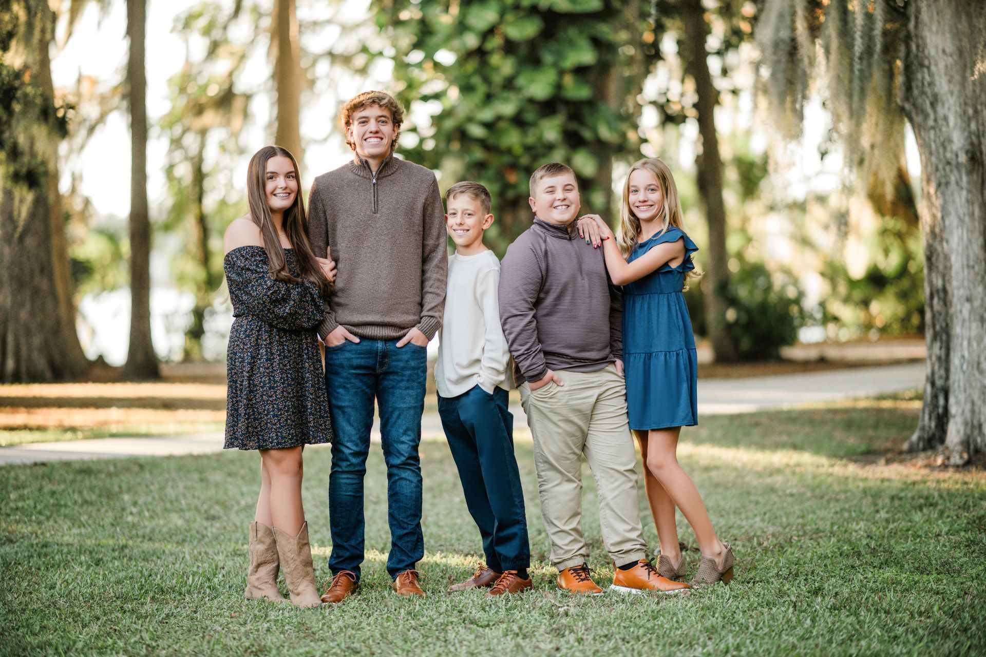 Five people standing together on a grassy lawn with trees in the background, smiling outdoors.