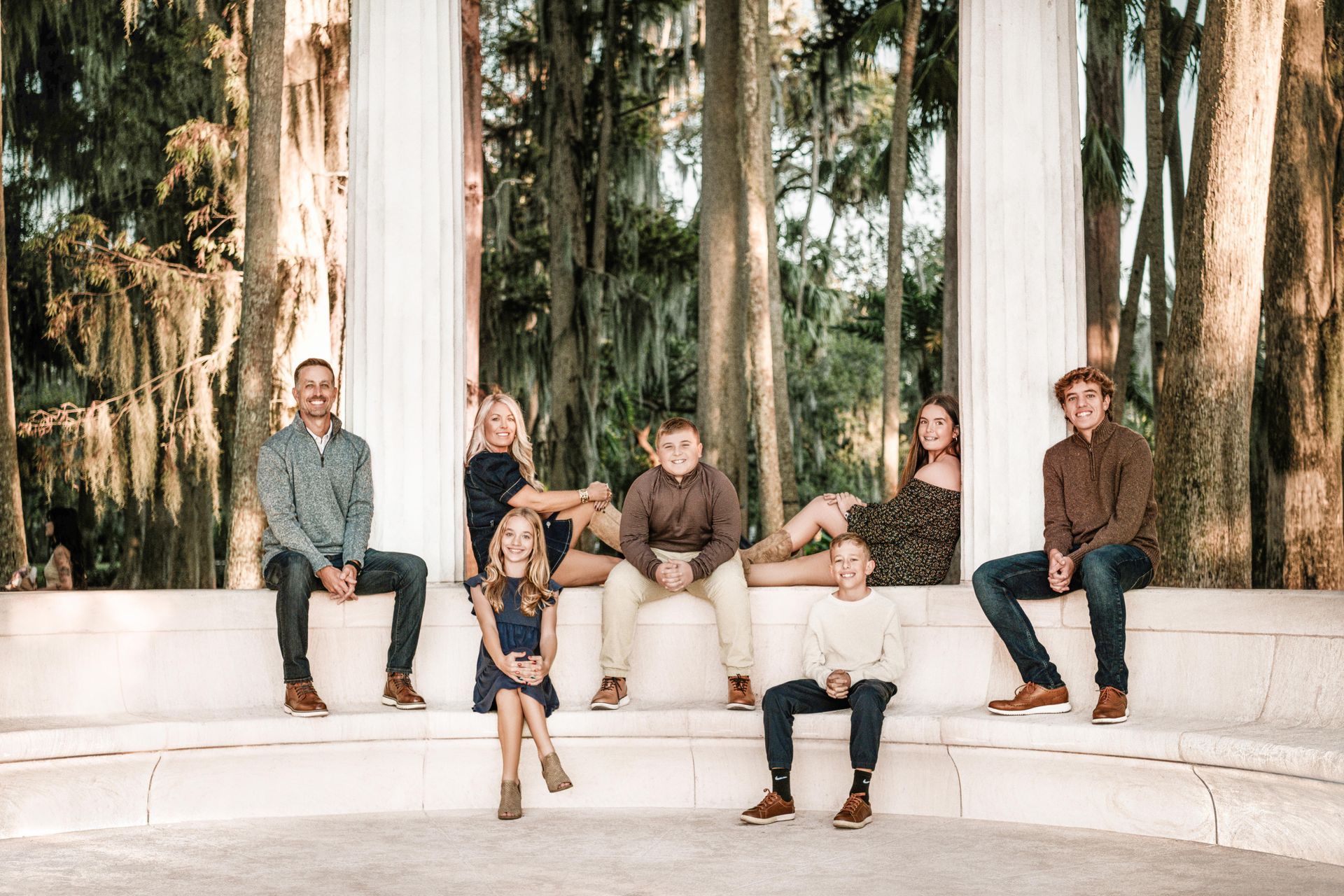 Five people sitting on white steps in a wooded outdoor setting with tall trees