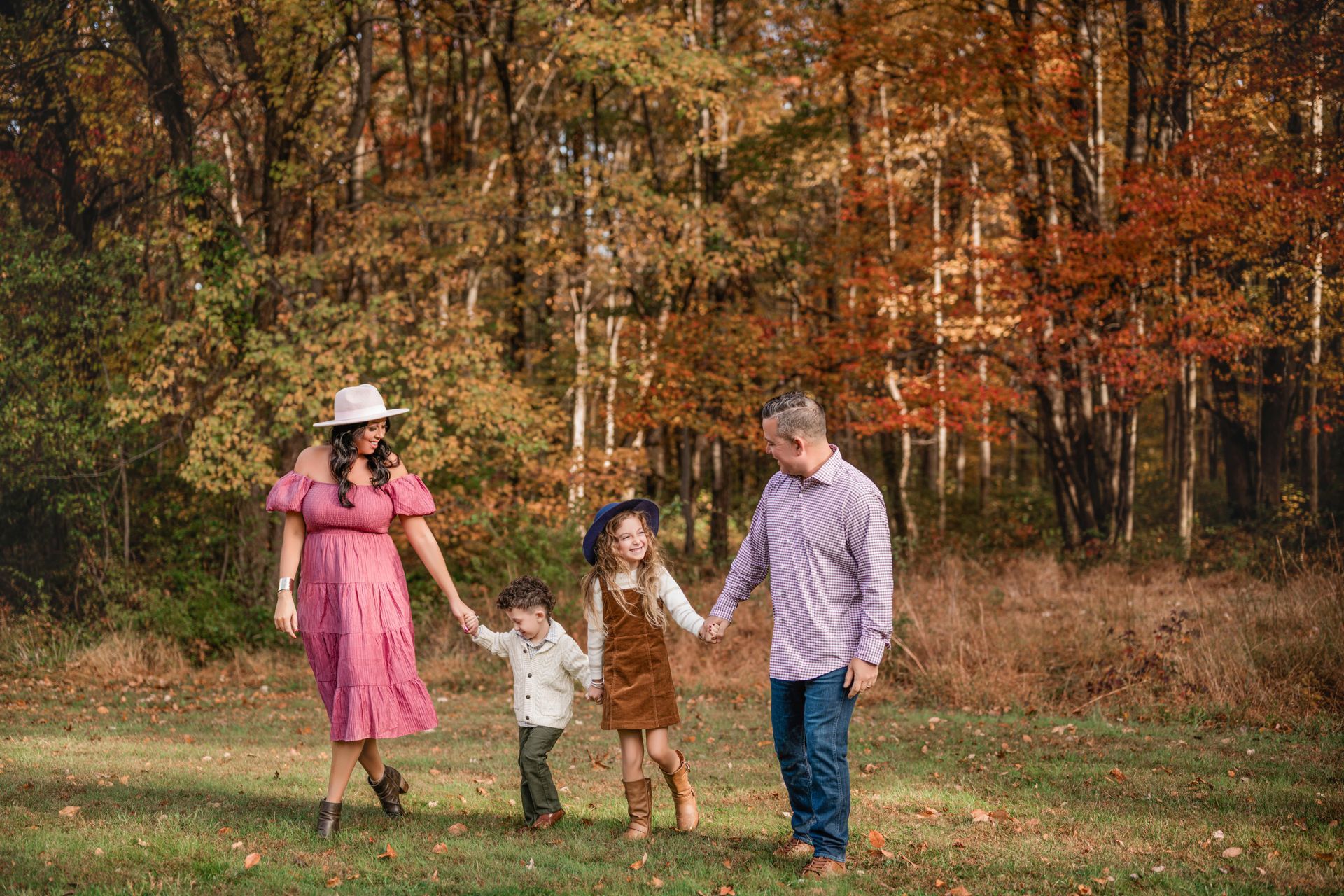 Four people holding hands and walking through a grassy park with autumn trees in the background