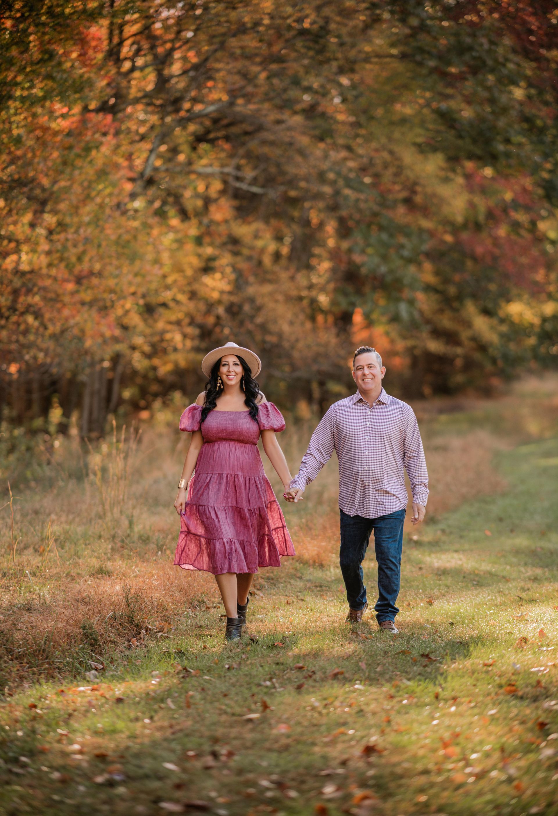 Two people walking hand in hand in a grassy park with autumn trees behind them