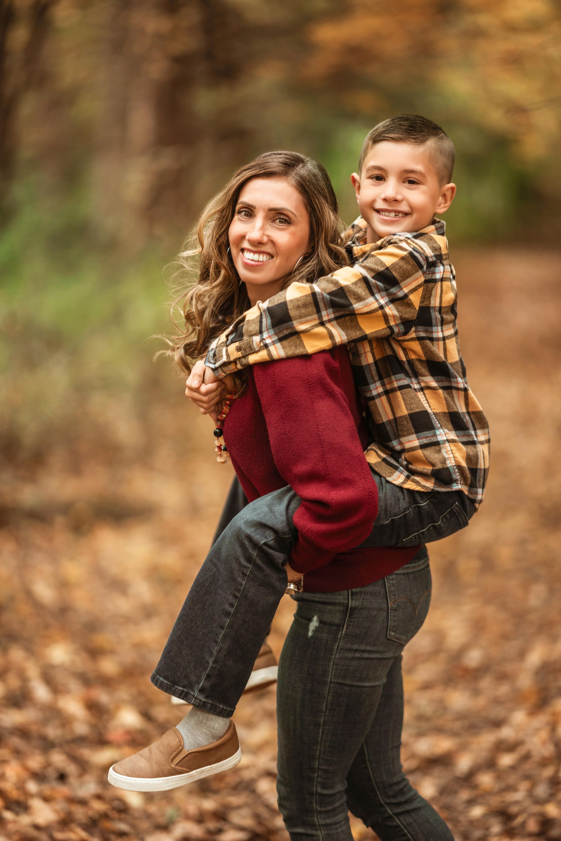 Two people hugging outdoors on a leaf-covered path in autumn, both smiling at the camera