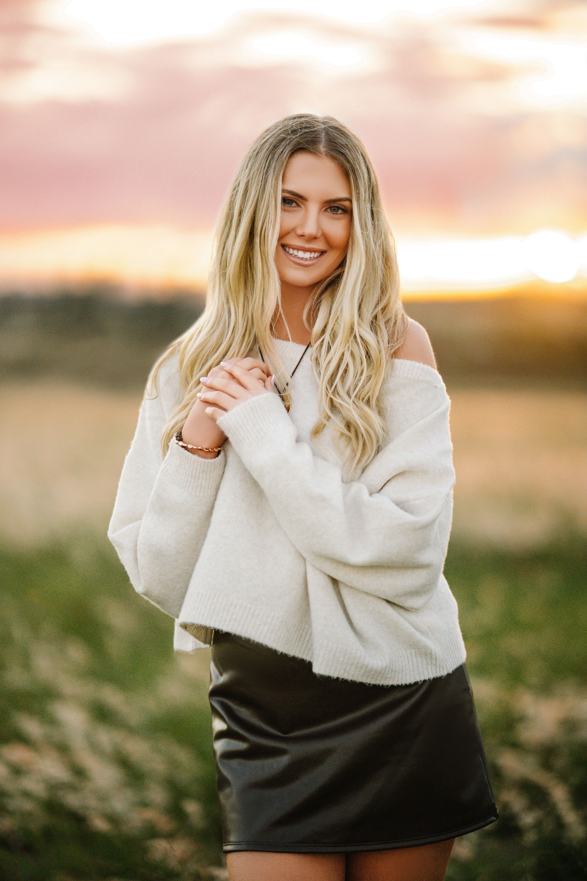 Woman in graduation cap and gown, smiling, outdoors on a wooden walkway.