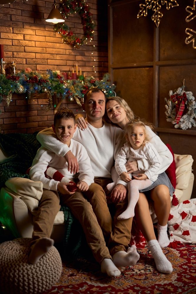 Family sitting together on a couch by a brick fireplace decorated for Christmas, smiling in cozy clothes