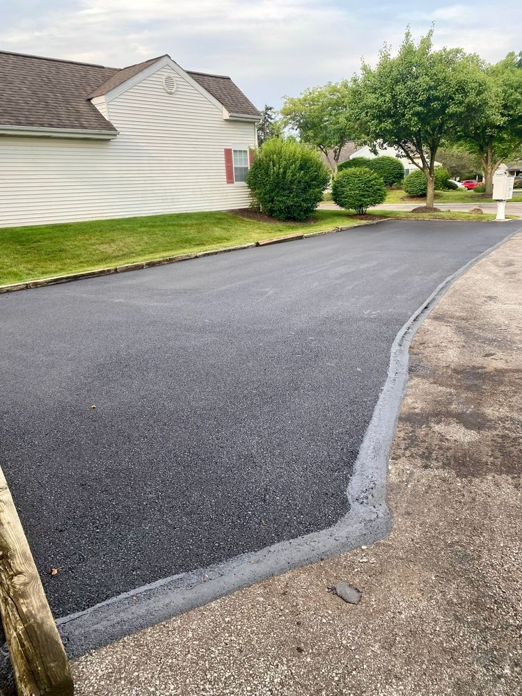 Freshly paved black driveway beside a white house and green lawn on a quiet residential street